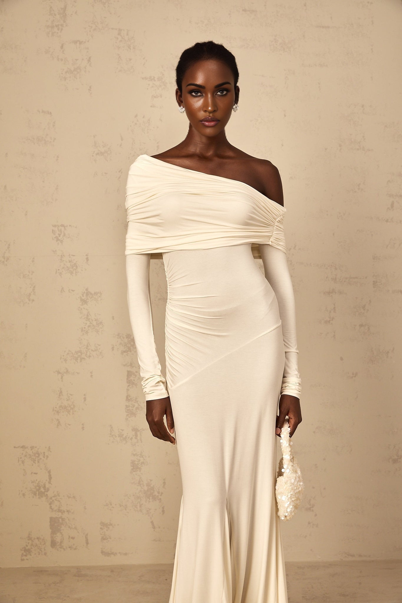 A woman wearing a white offshoulder maxi dress with ruched detailing standing in a relaxed pose