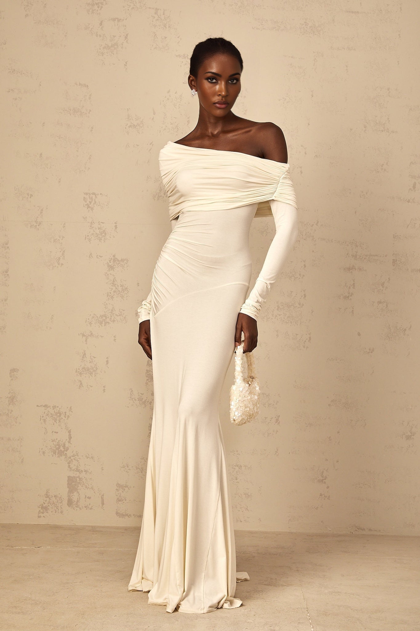 A woman wearing a white offshoulder maxi dress with ruched detailing standing in a relaxed pose