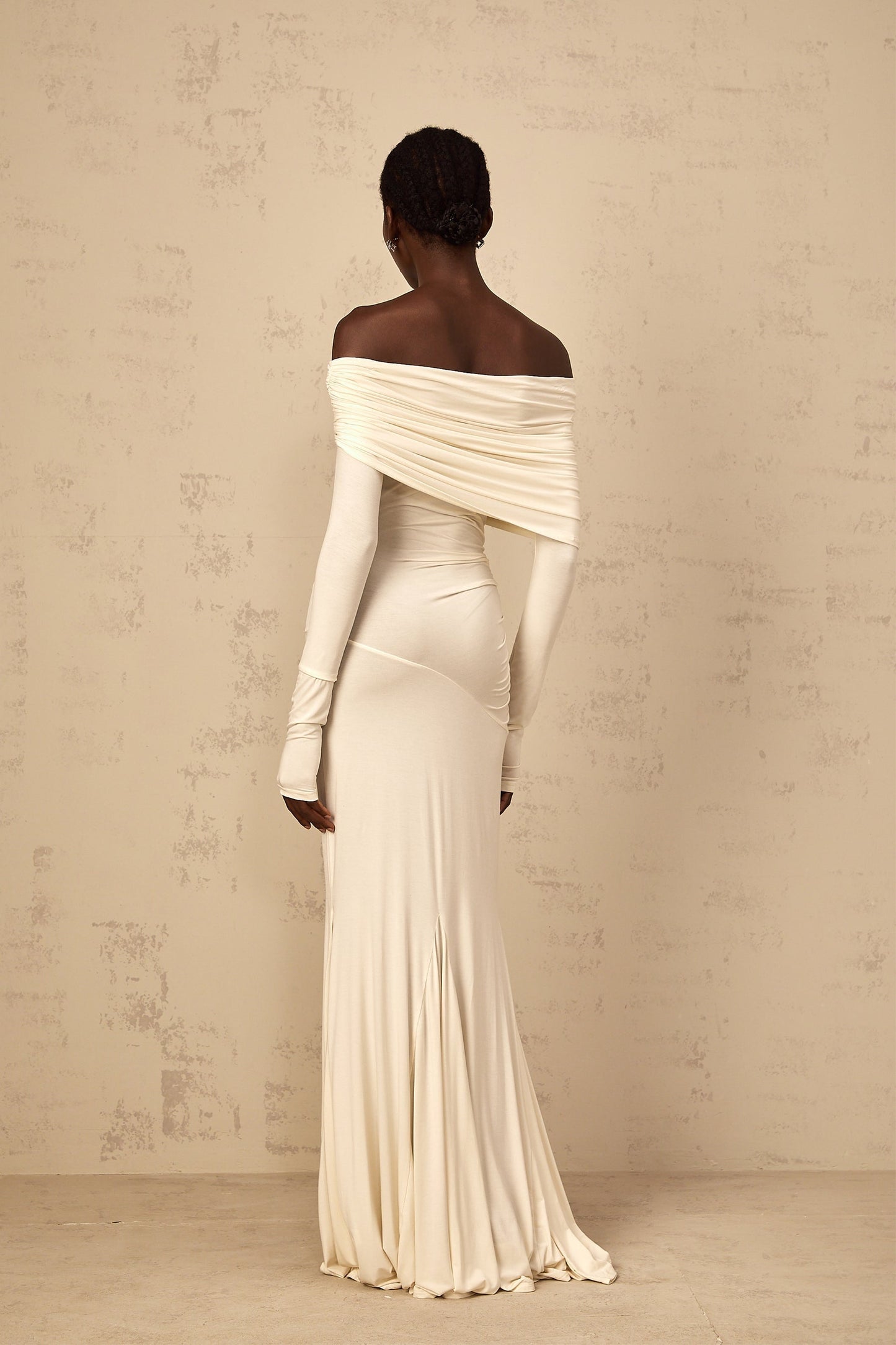 A woman wearing a white offshoulder maxi dress with ruched detailing standing in a relaxed pose