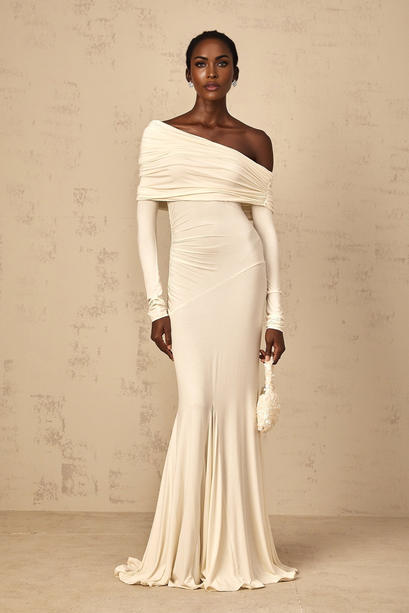 A woman wearing a white offshoulder maxi dress with ruched detailing standing in a relaxed pose