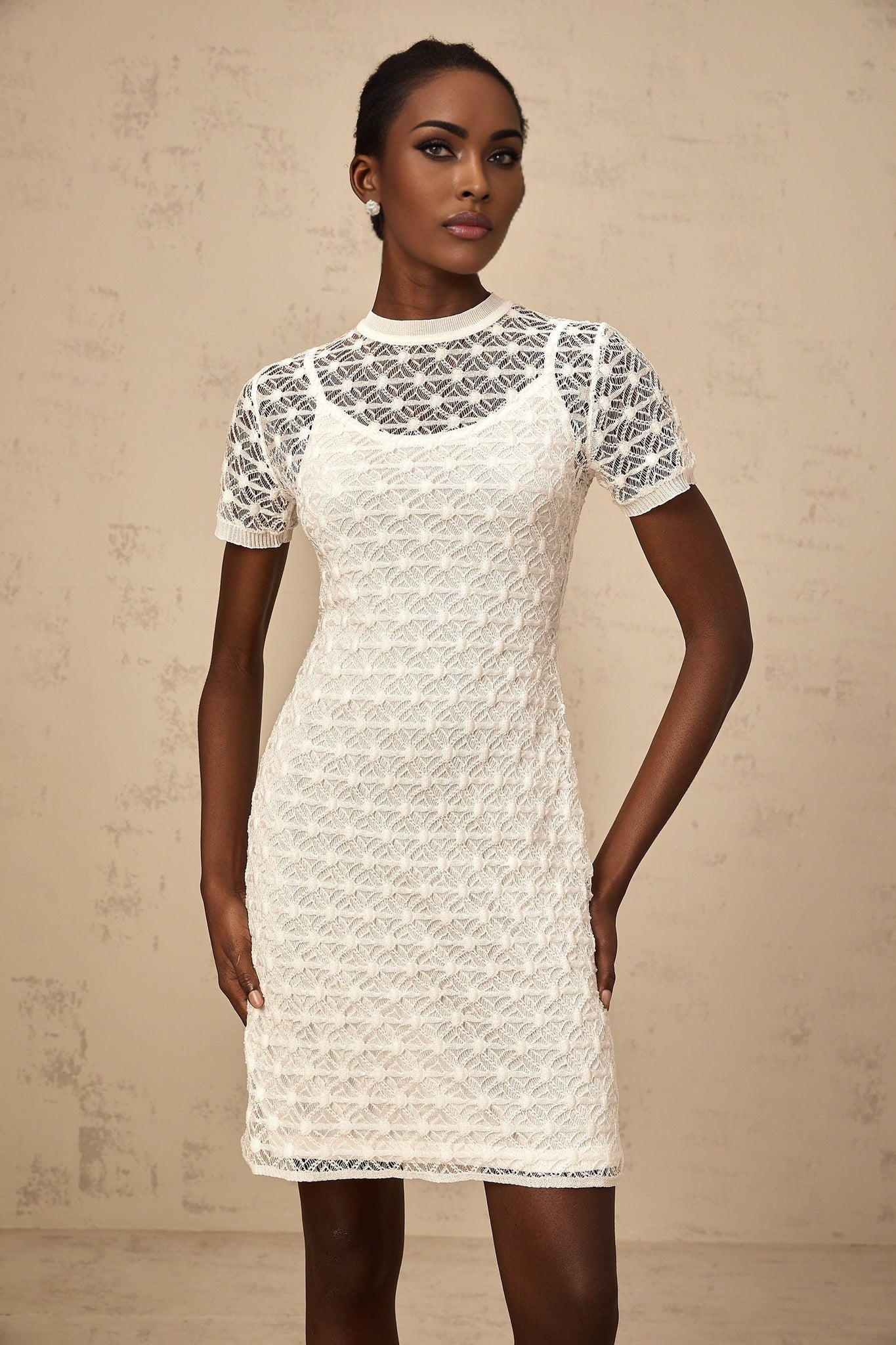 A woman wearing a white semisheer knit mini dress standing in a casual pose