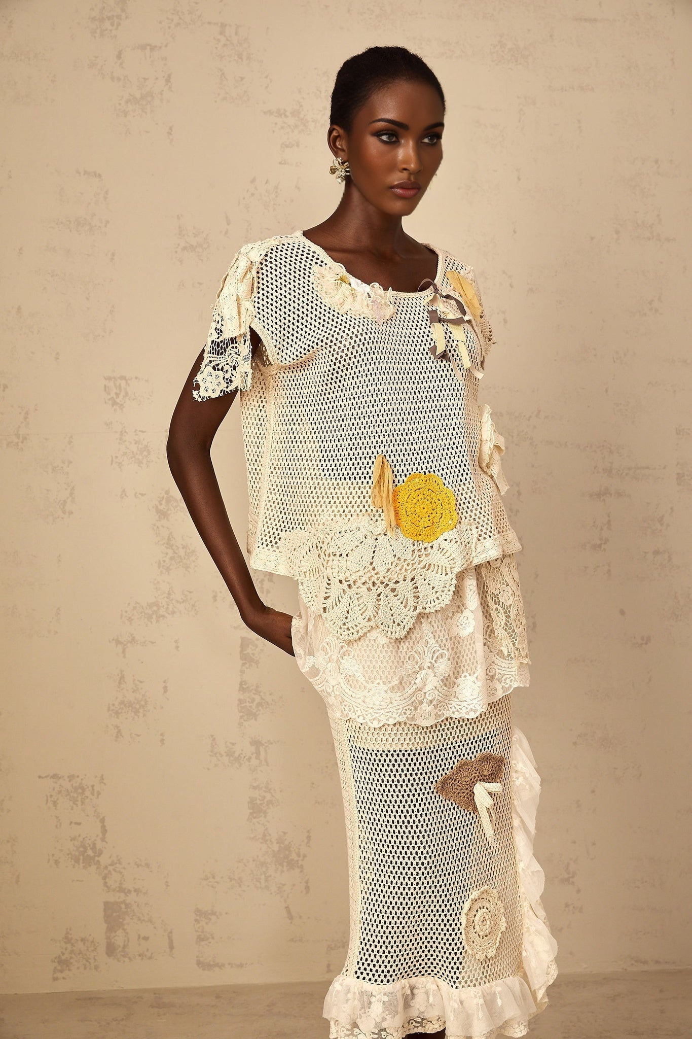 A woman wearing a white sleeveless top with intricate lace panels and crochet knit details