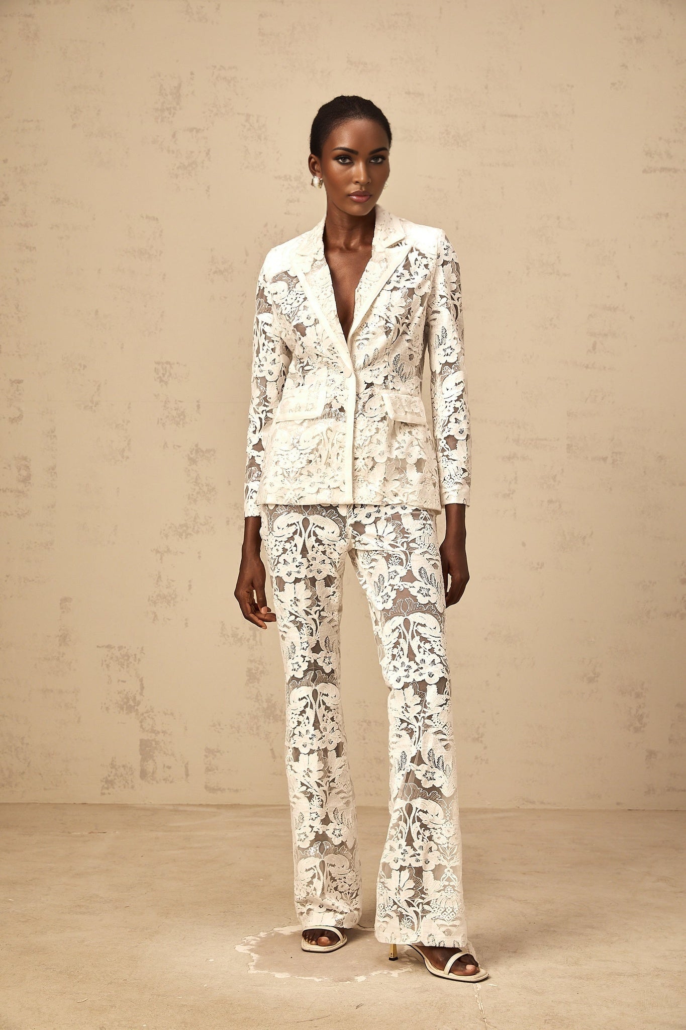 A woman wearing a white tulle blazer and matching trousers adorned with sequined flower embroidery The outfit is a coordinated set with a delicate and elegant appearance