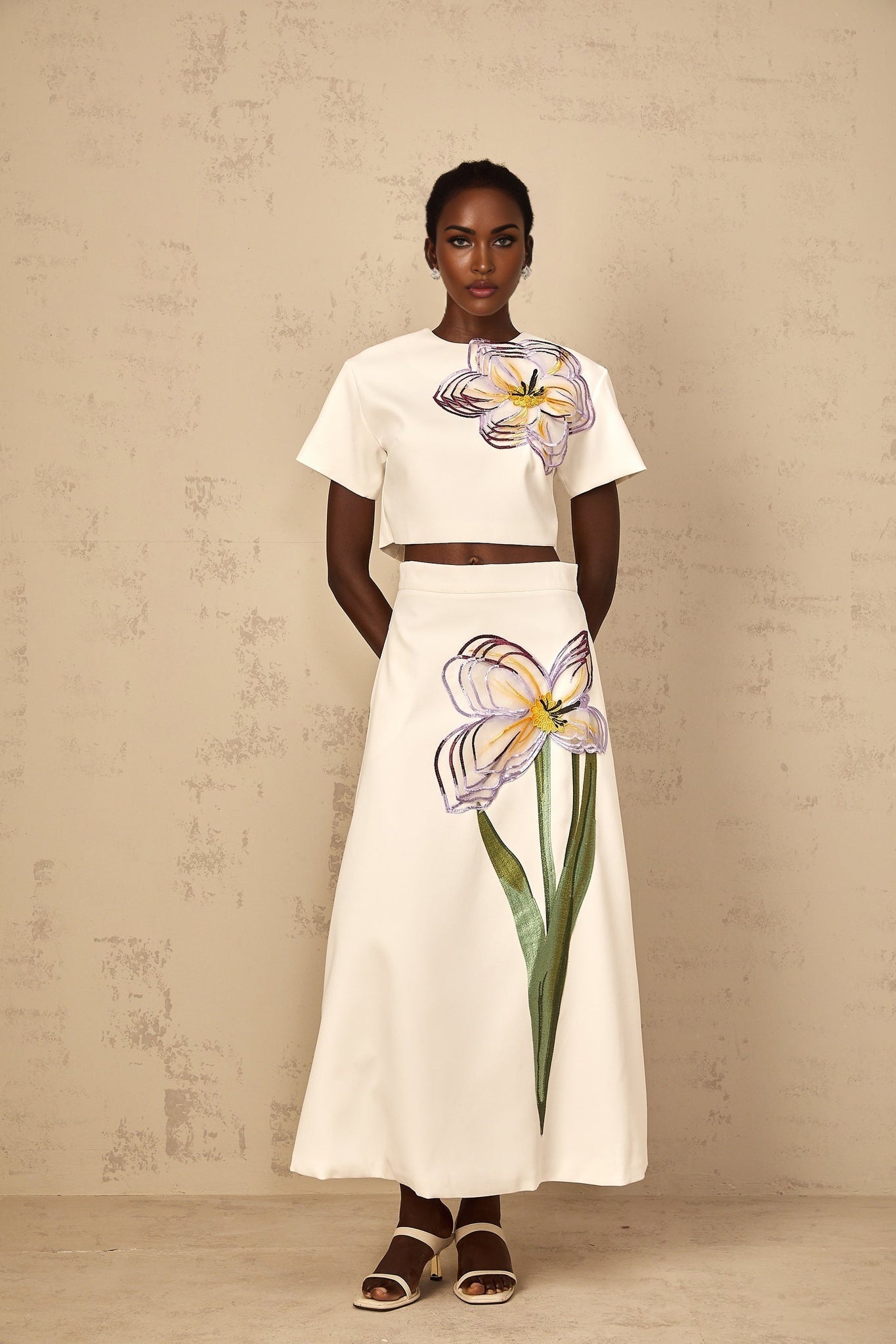 A woman wearing a white two piece outfit featuring sequin floral embroidery on both the top and bottom pieces of the matching set