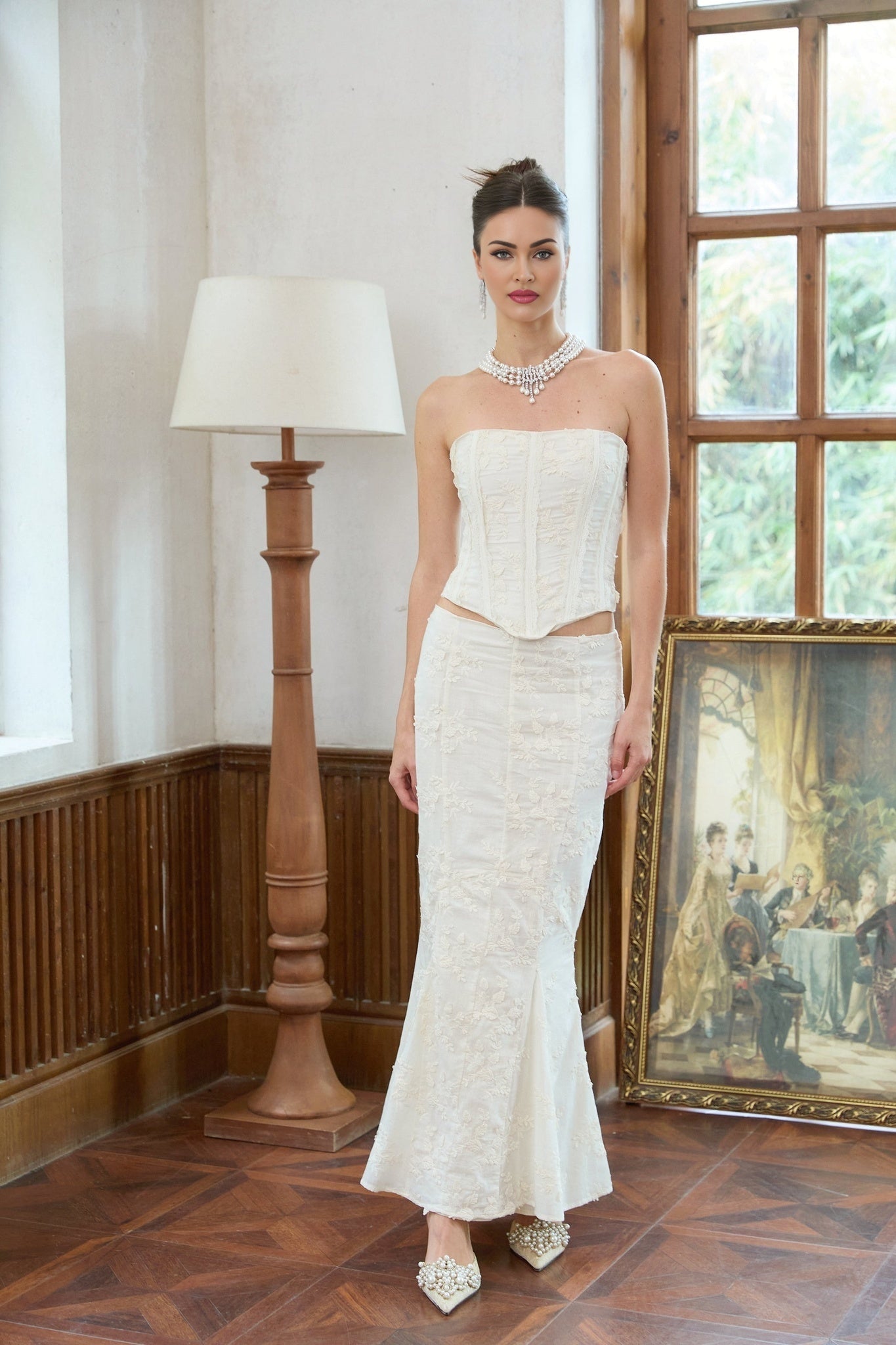 A woman wearing a white twopiece outfit consisting of an embroidered crop top and matching skirt with floral embroidery details