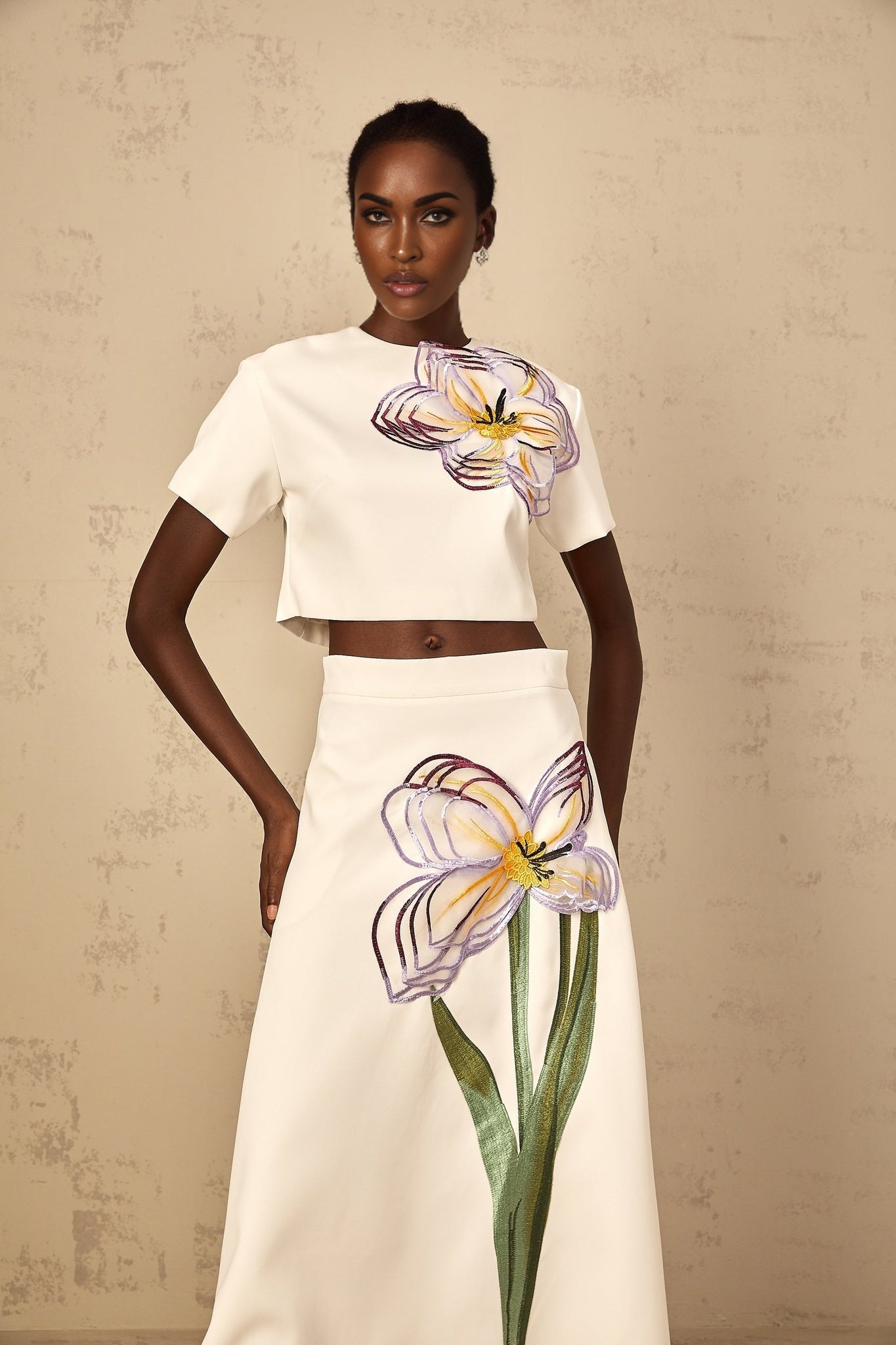 A woman wearing a white twopiece outfit featuring sequin floral embroidery on both the top and bottom garments