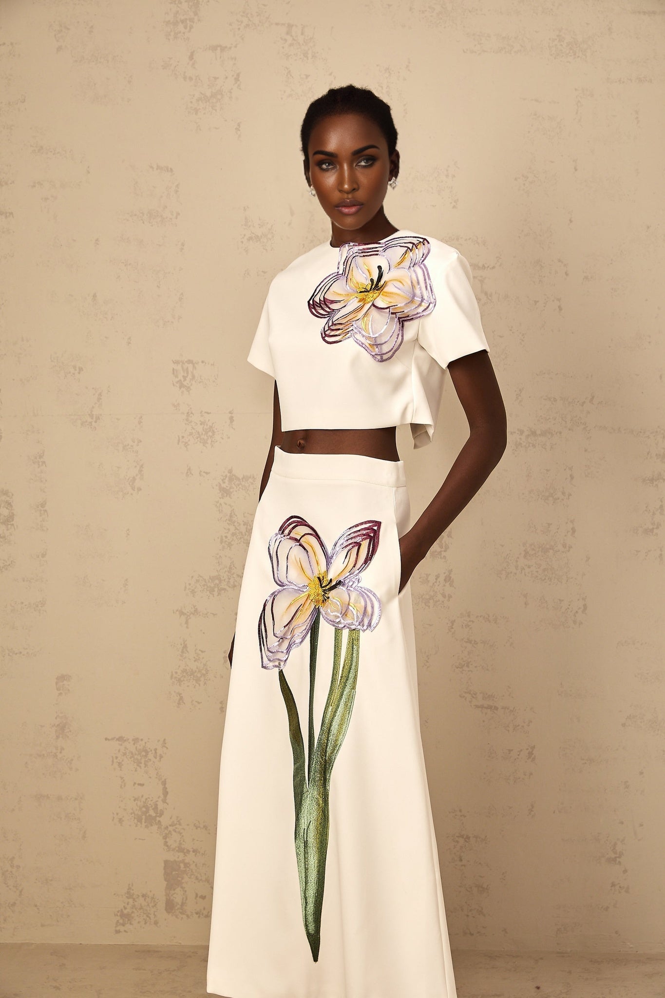 A woman wearing a white twopiece outfit featuring sequin floral embroidery on both the top and bottom halves of the matching set