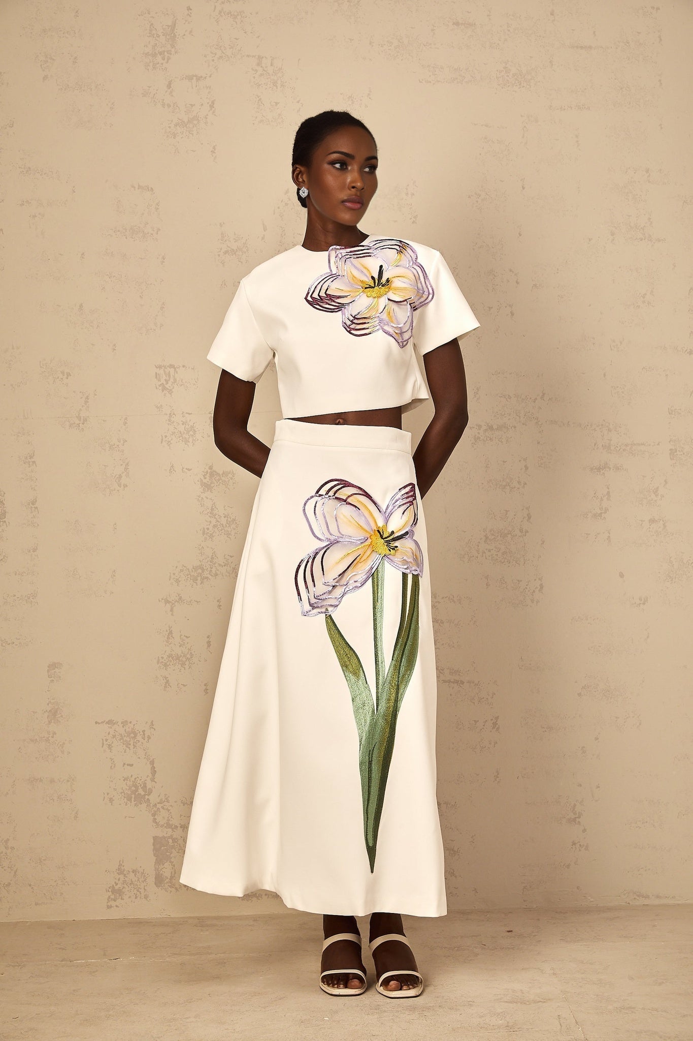 A woman wearing a white twopiece outfit featuring sequin floral embroidery on both the top and bottom pieces of the matching set