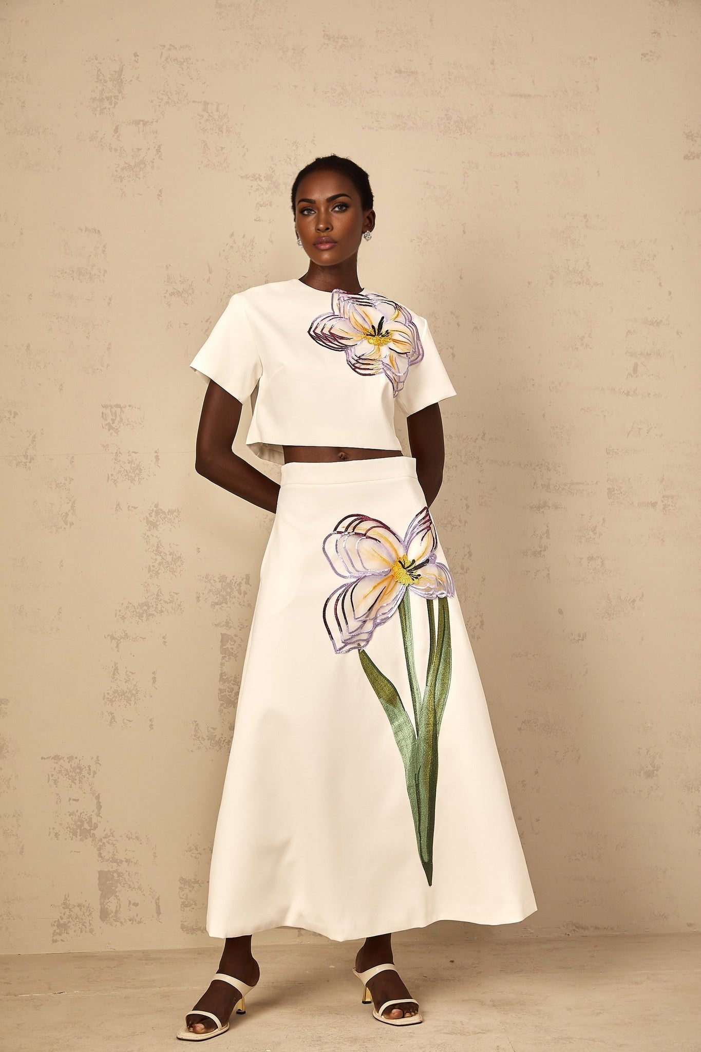 A woman wearing a white twopiece outfit featuring sequin floral embroidery on both the top and bottom pieces of the matching set