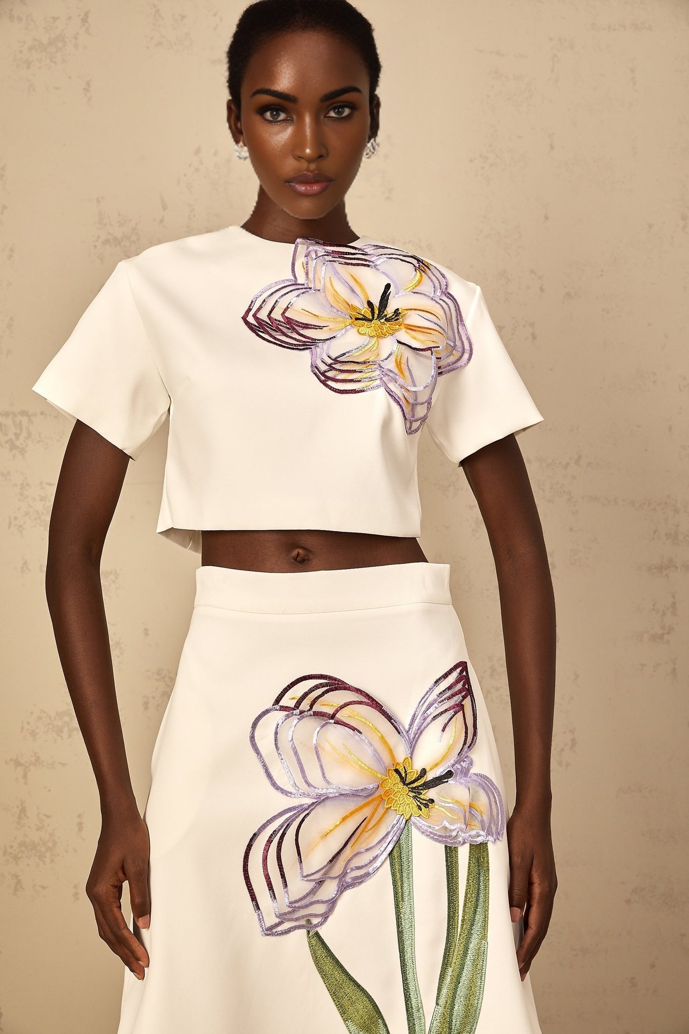 A woman wearing a white twopiece outfit featuring sequin floral embroidery on both the top and bottom pieces of the matching set