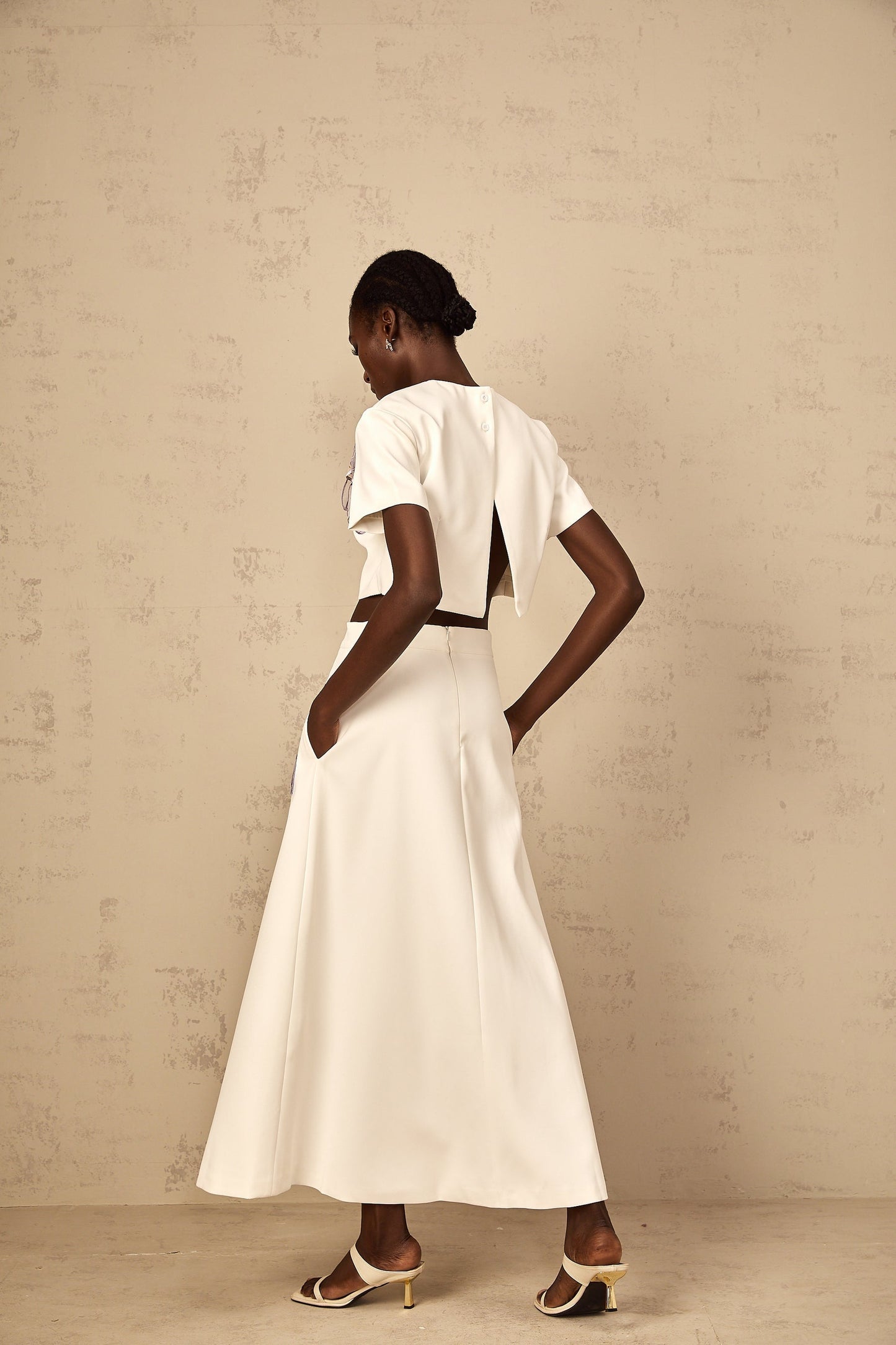 A woman wearing a white twopiece outfit with sequin floral embroidery consisting of a cropped top and matching bottoms
