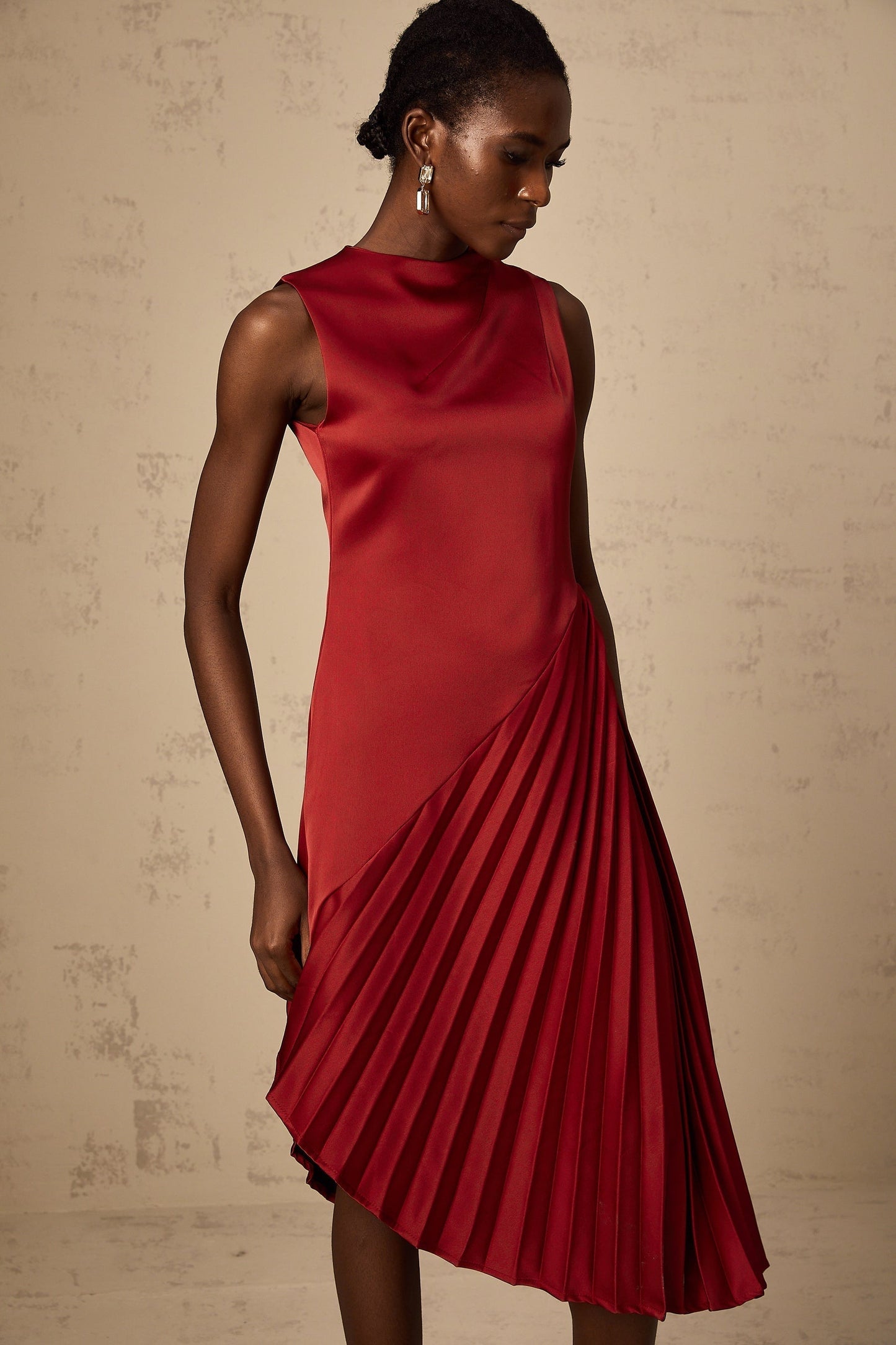A woman wearing a wine red midi dress with an asymmetric neckline and pleated skirt detail