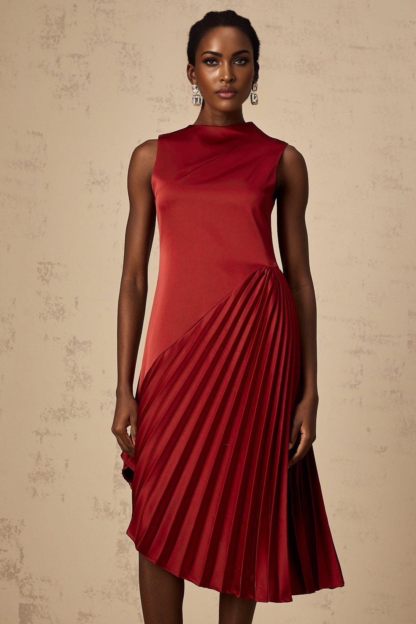 A woman wearing a wine red pleated midi dress with an asymmetric hemline and flowing silhouette