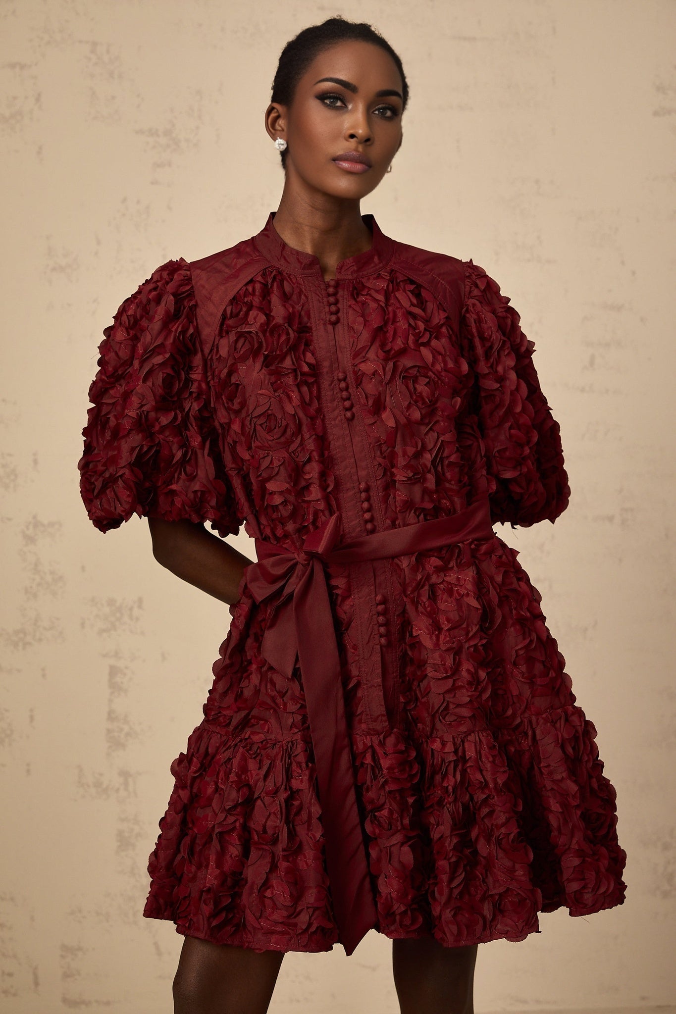 A woman wearing a winered mini dress with three dimensional petal shaped puffs covering the fabric creating a textured floral look