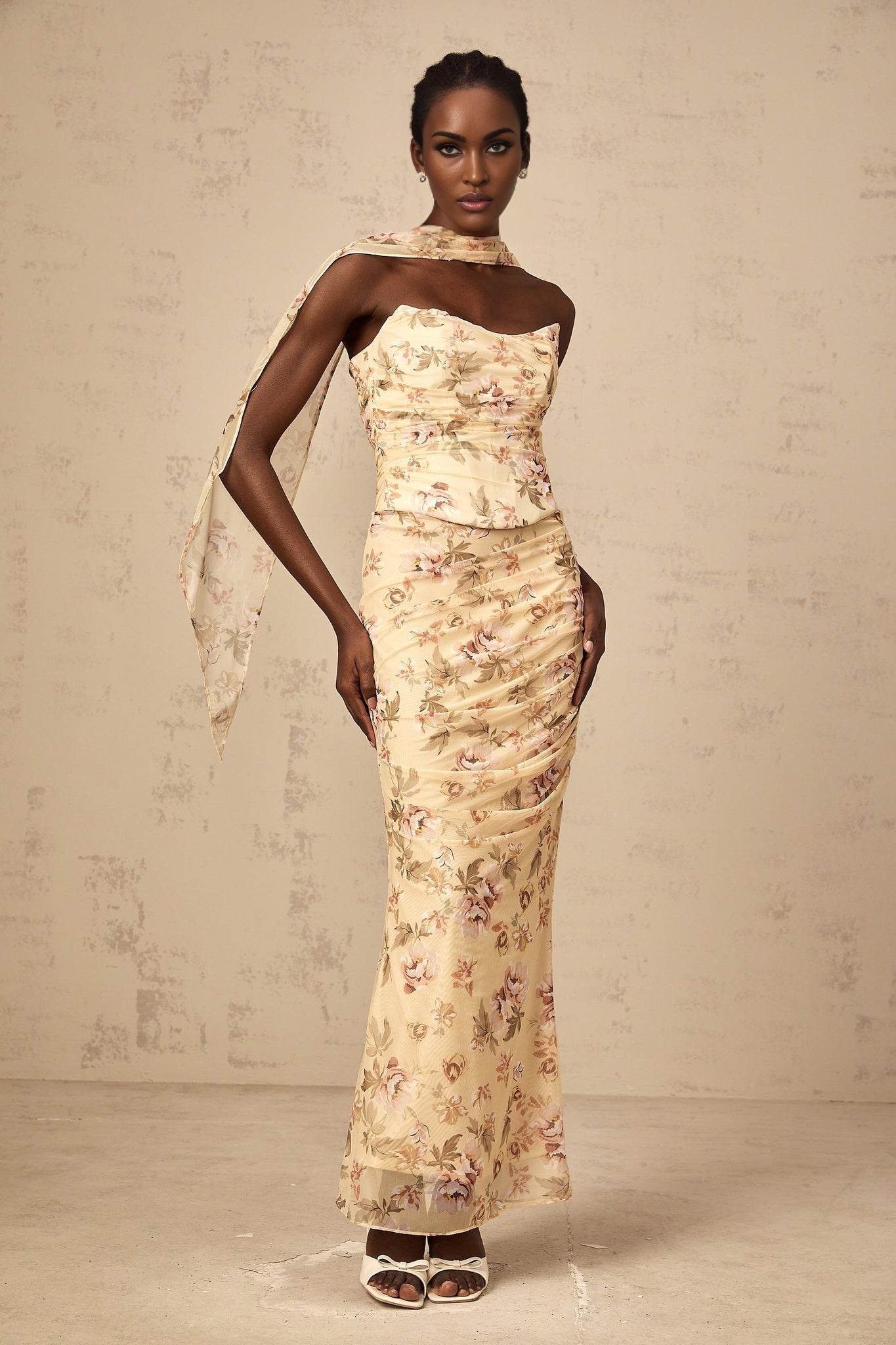 A woman wearing a yellow floral print matching set consisting of a fitted top and skirt standing against a plain background