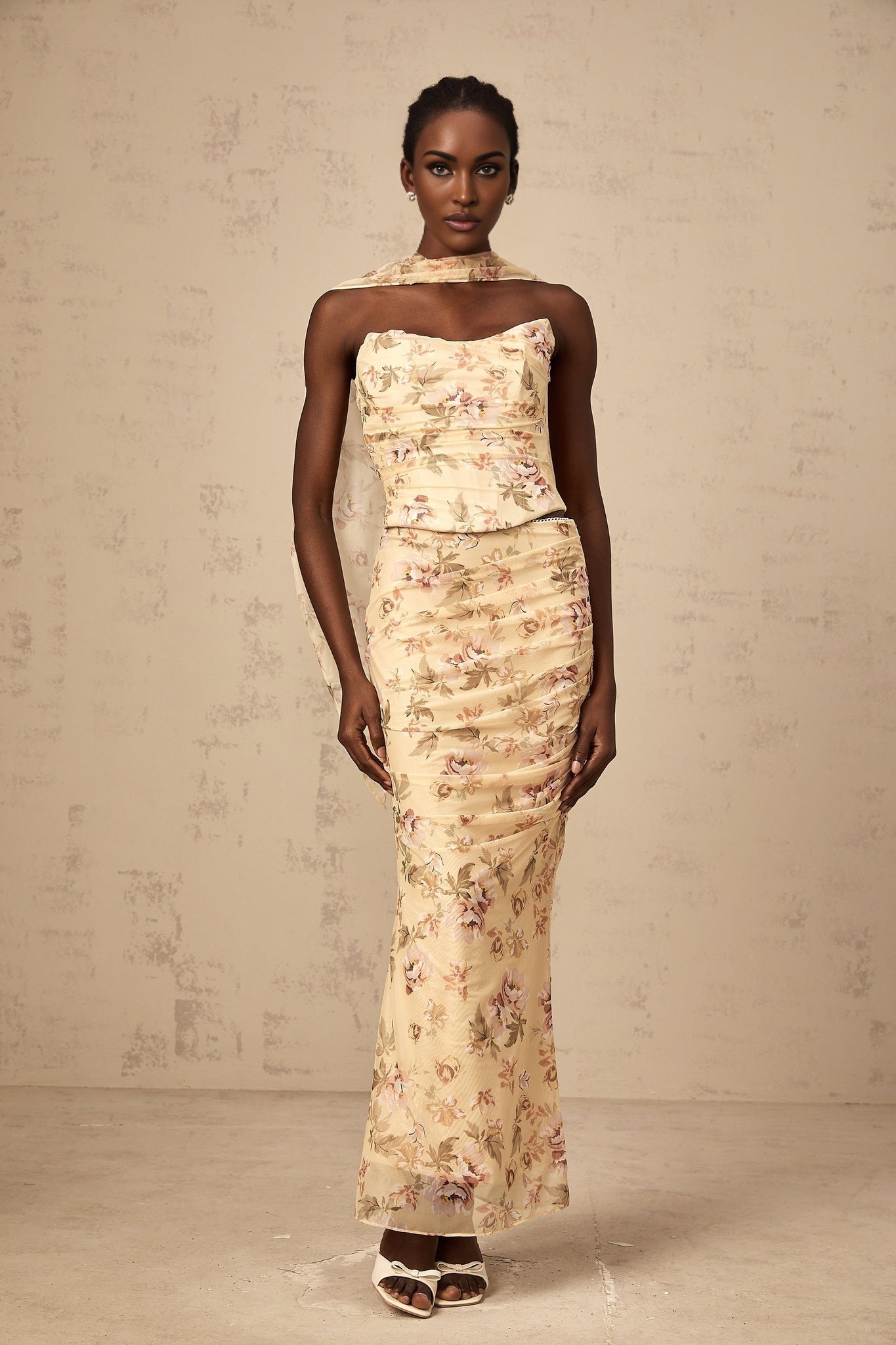 A woman wearing a yellow floral print matching set consisting of a fitted top and skirt with a vibrant summery design