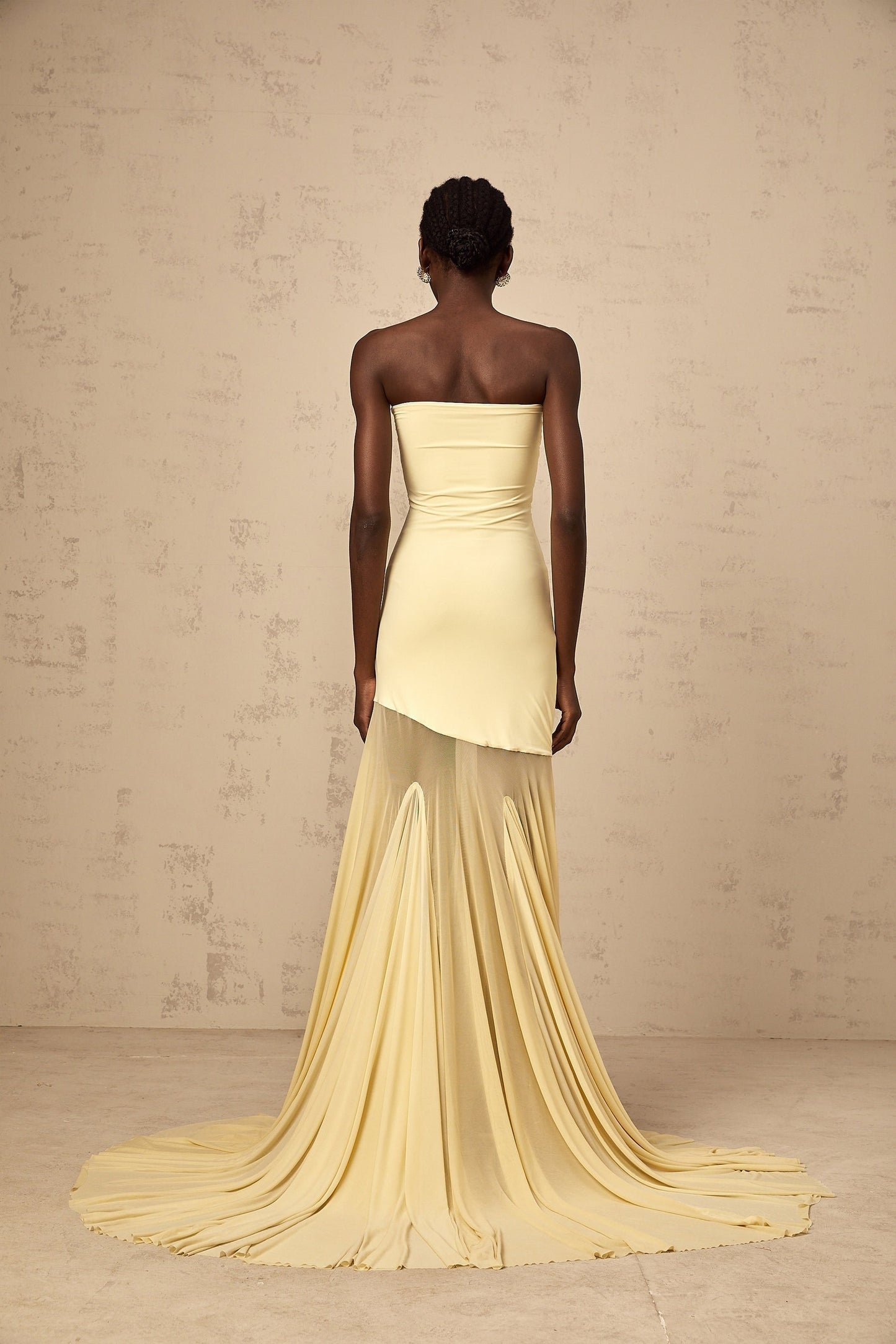 A woman wearing a yellow offshoulder maxi dress with sheer tulle fabric standing against a plain background