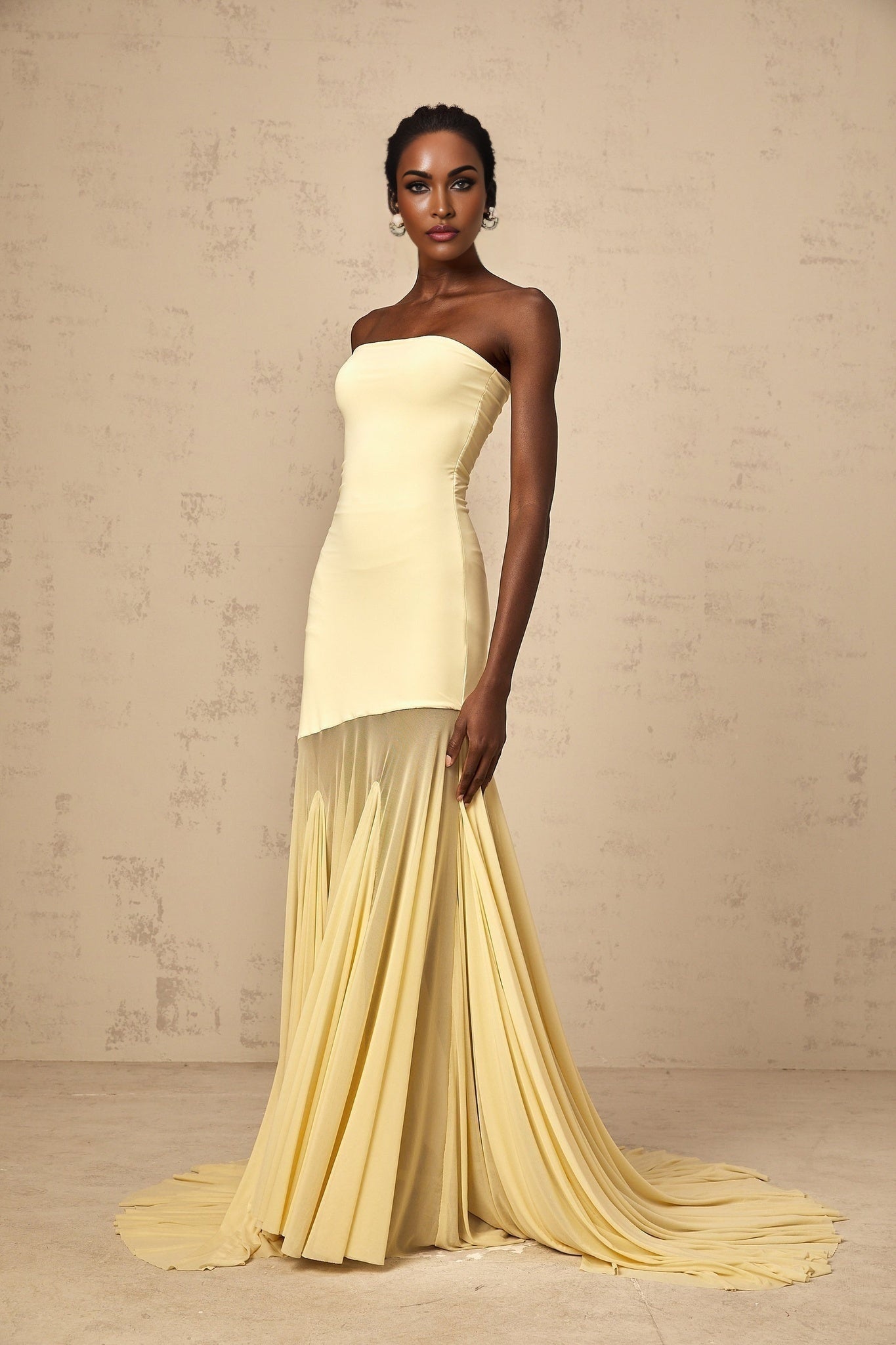 A woman wearing a yellow offshoulder maxi dress with sheer tulle fabric standing against a plain background