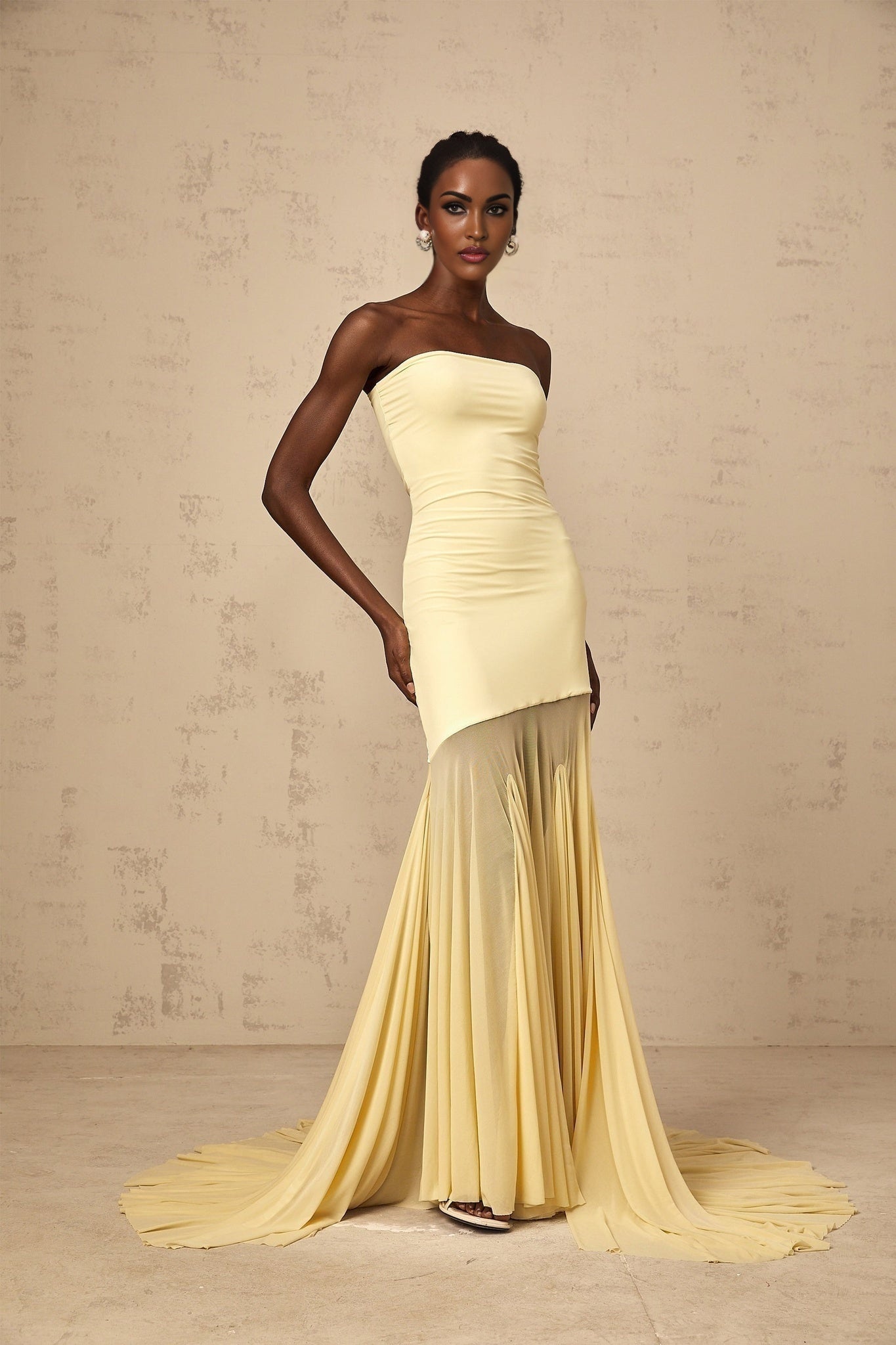 A woman wearing a yellow offshoulder maxi dress with sheer tulle overlay standing against a plain background