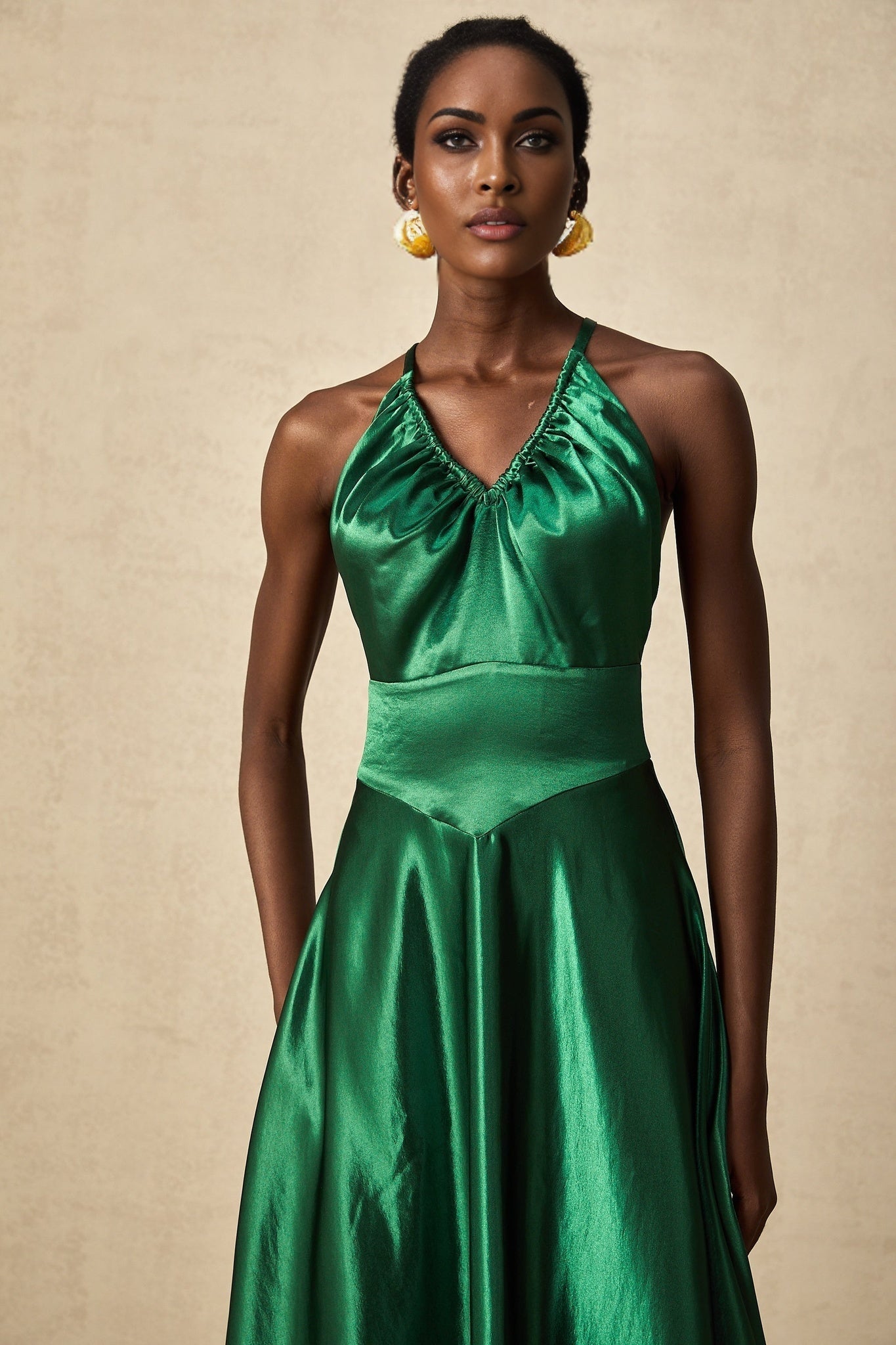 A woman wearing an emerald green satin midi dress with an open back design