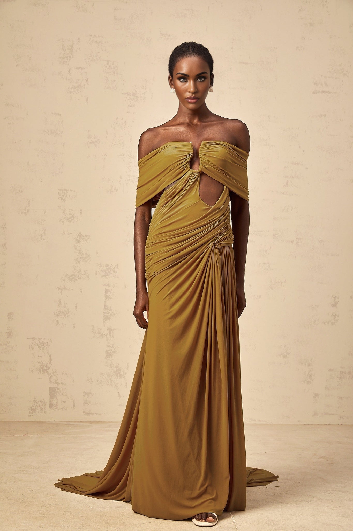A woman wearing an ocher off shoulder maxi dress with ruched details and a cut out design standing in a relaxed pose