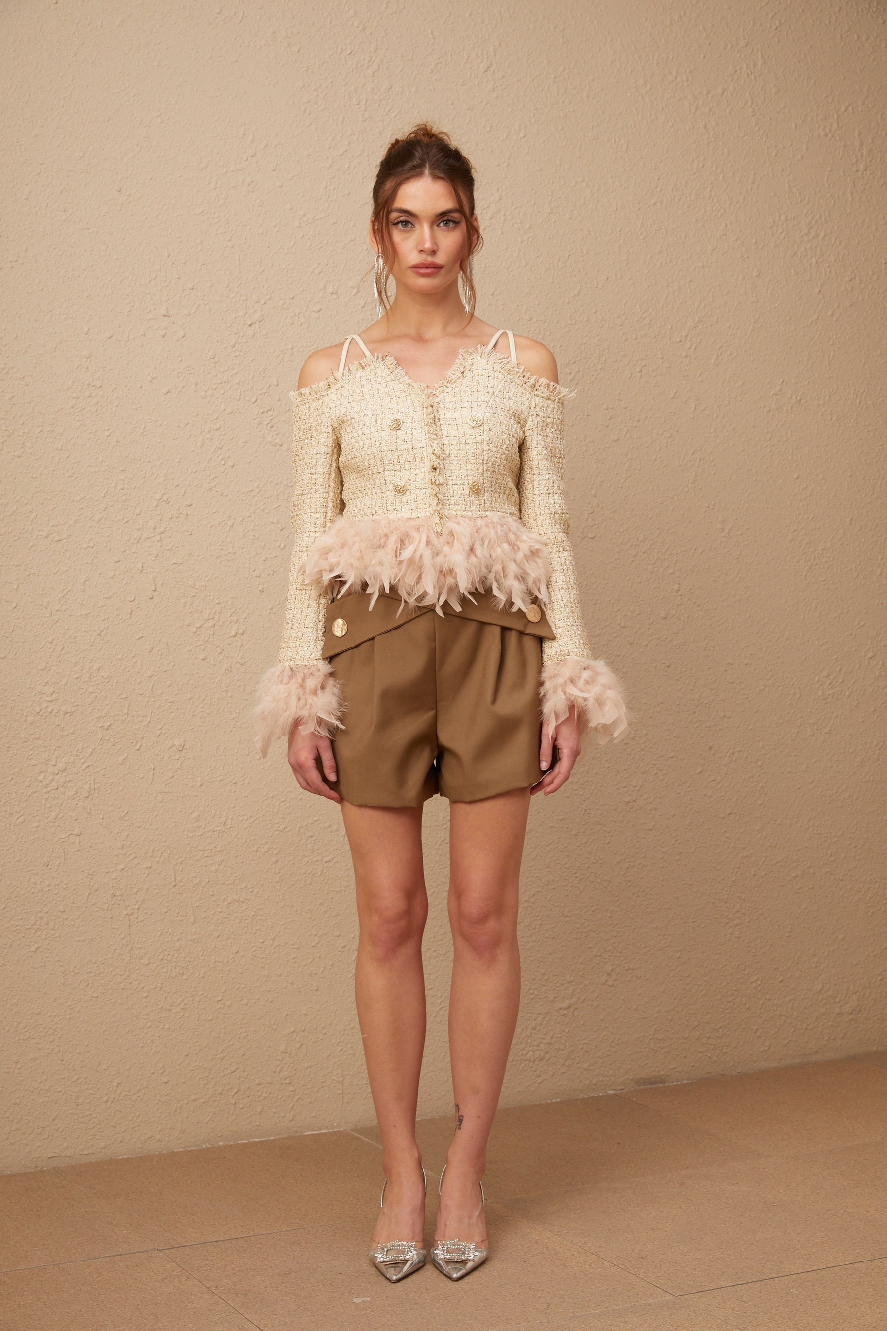 A woman wearing an offshoulder tweed top with feather trim around the neckline The top is fitted and has a textured tweed fabric in a neutral color The feather trim adds a luxurious and elegant touch to the garment
