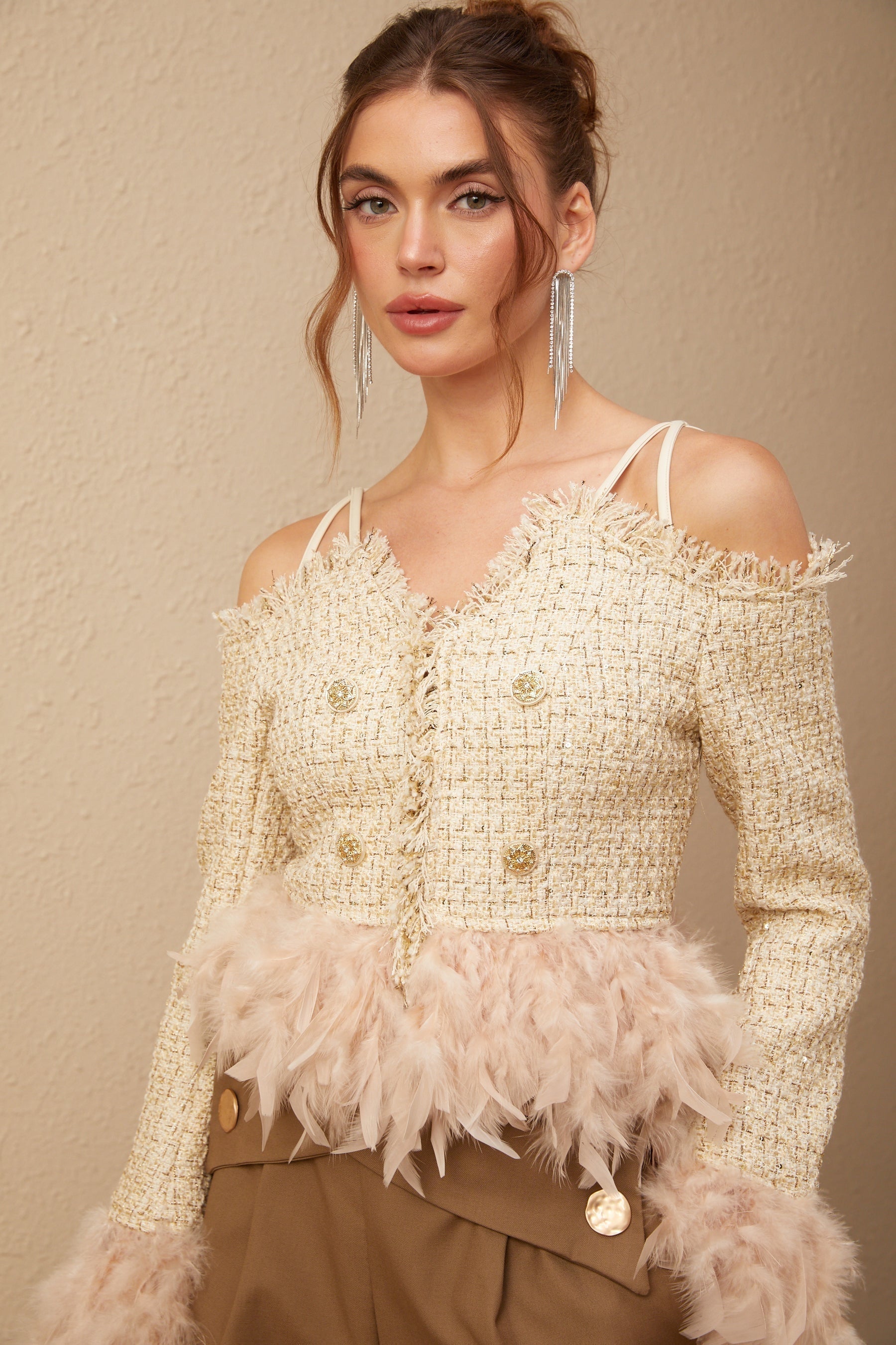 A woman wearing an offshoulder tweed top with feather trim around the neckline The top is fitted and has a textured tweed fabric in neutral tones The feather trim adds a luxurious and elegant touch to the garment