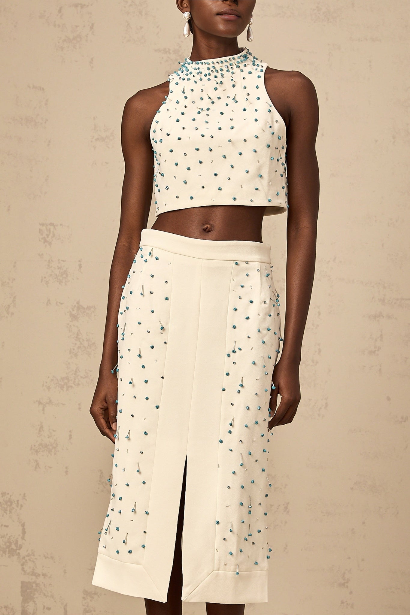A woman wearing an offwhite matching set consisting of an embellished top and skirt named Clothilde The top features delicate embroidery while the skirt has a flowing design Both pieces are coordinated in color and style creating an elegant ensemble