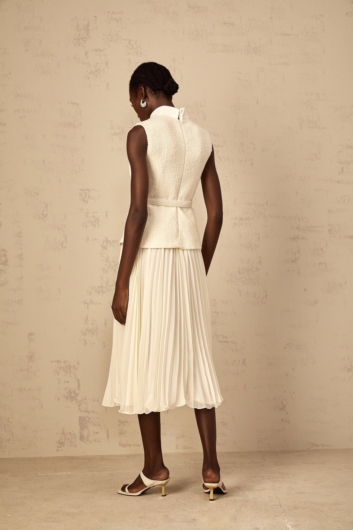 A woman wearing an offwhite midi dress with a tweed bodice and tulle panel skirt standing in a neutral background
