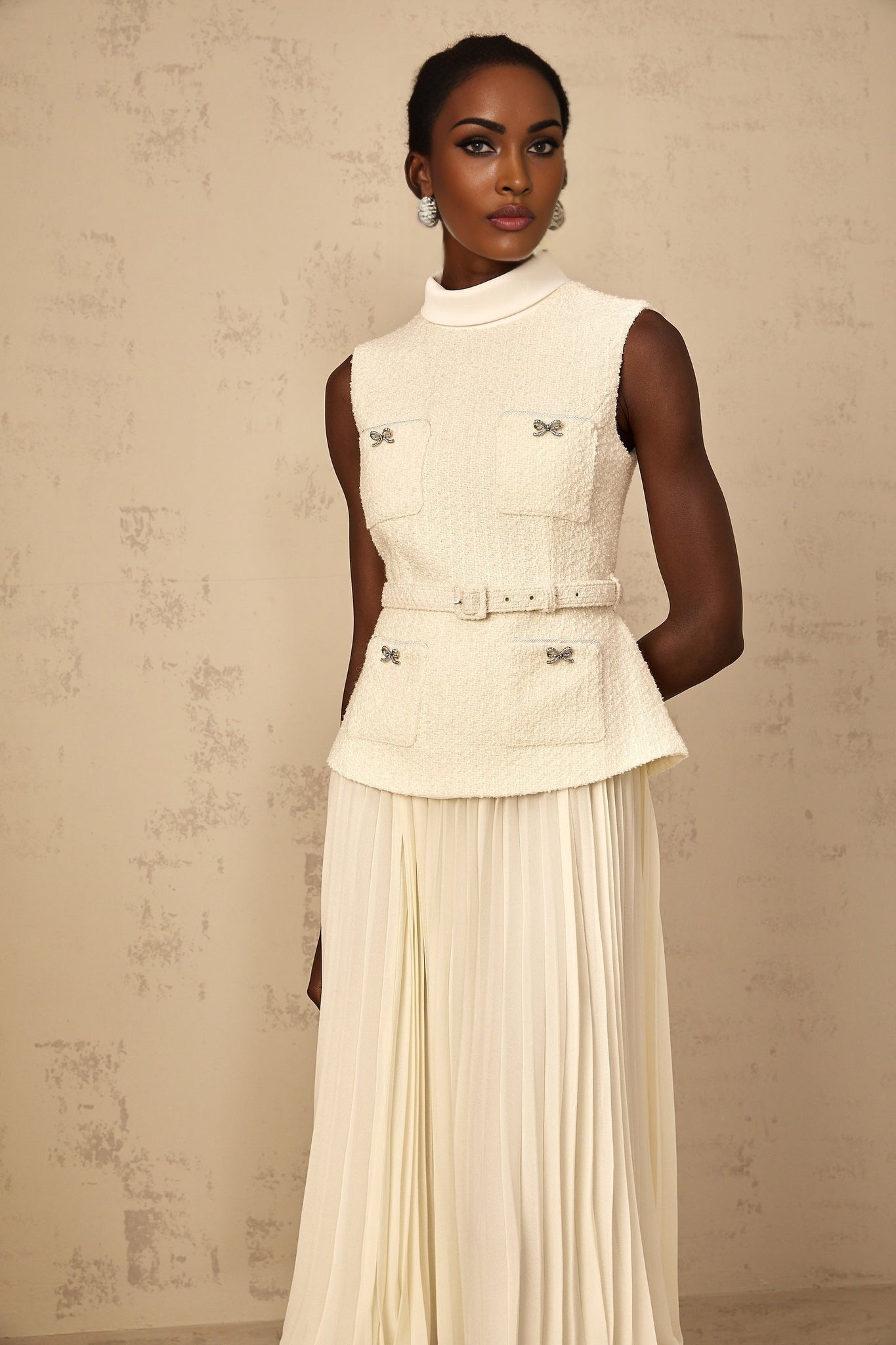 A woman wearing an offwhite midi dress with a tweed fabric body and tulle panel details standing in a neutral background