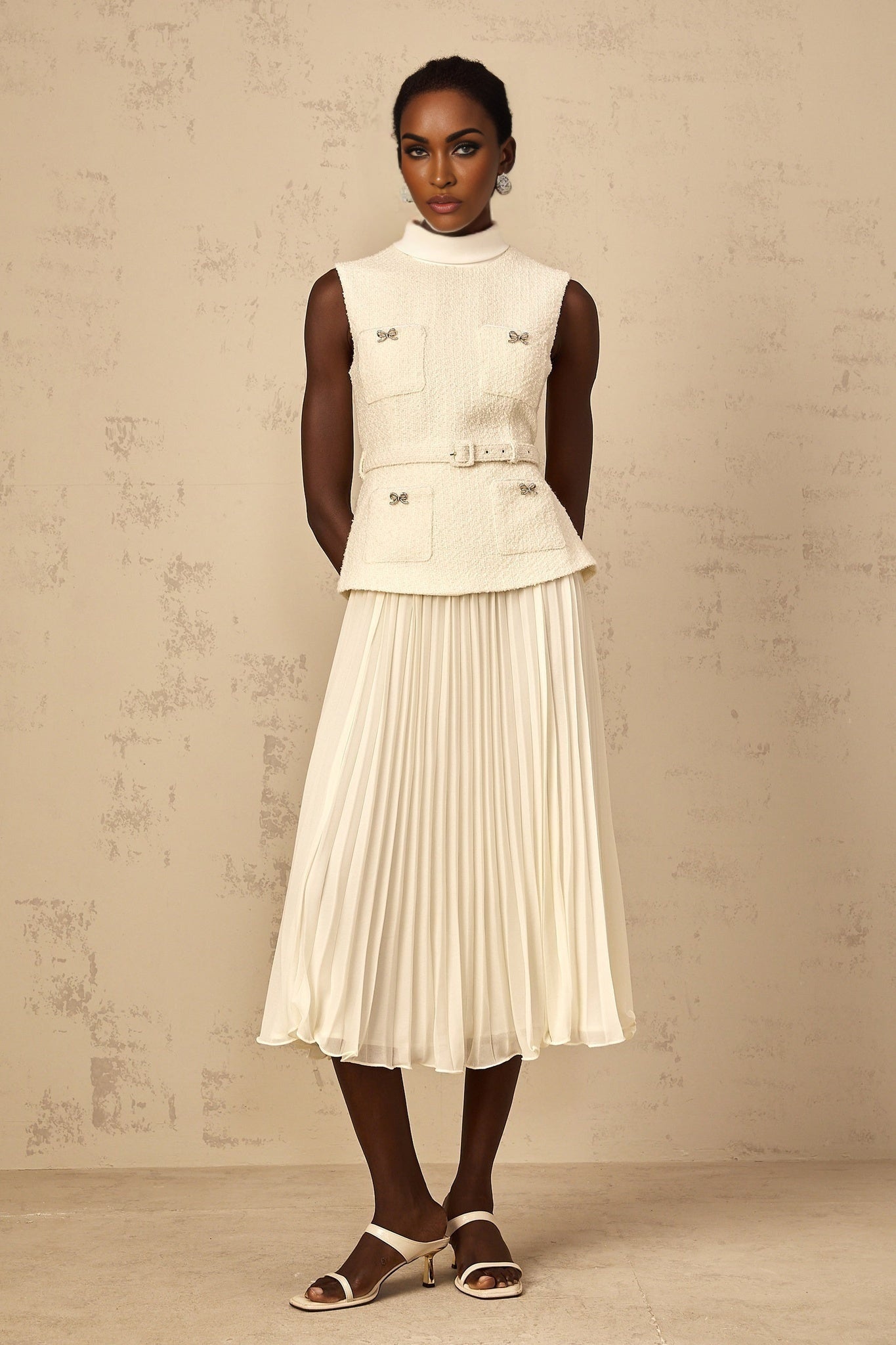 A woman wearing an offwhite midi dress with tweed fabric and tulle panel details standing in a neutral background