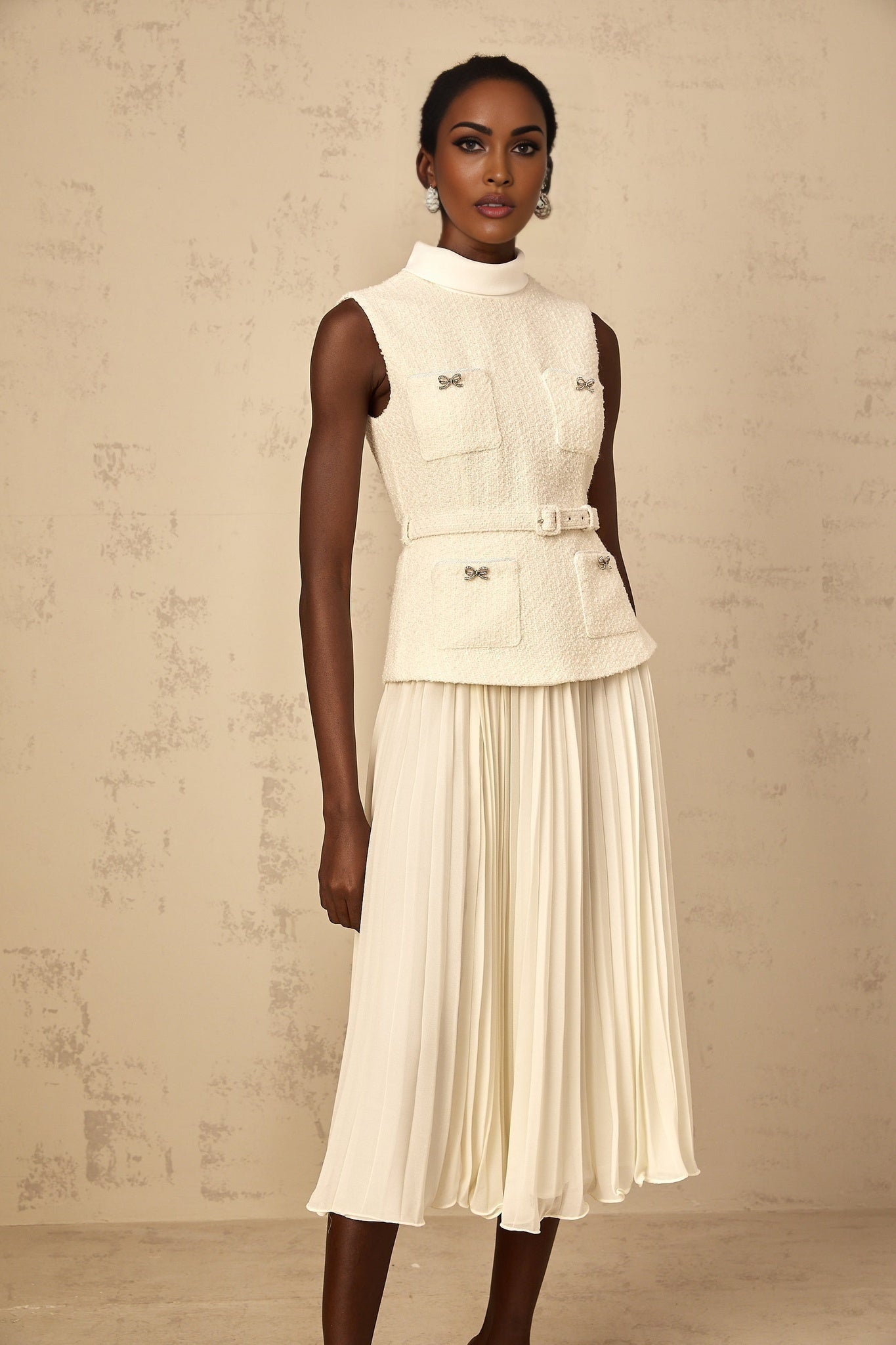 A woman wearing an offwhite midi dress with tweed fabric and tulle panel details standing in a neutral background