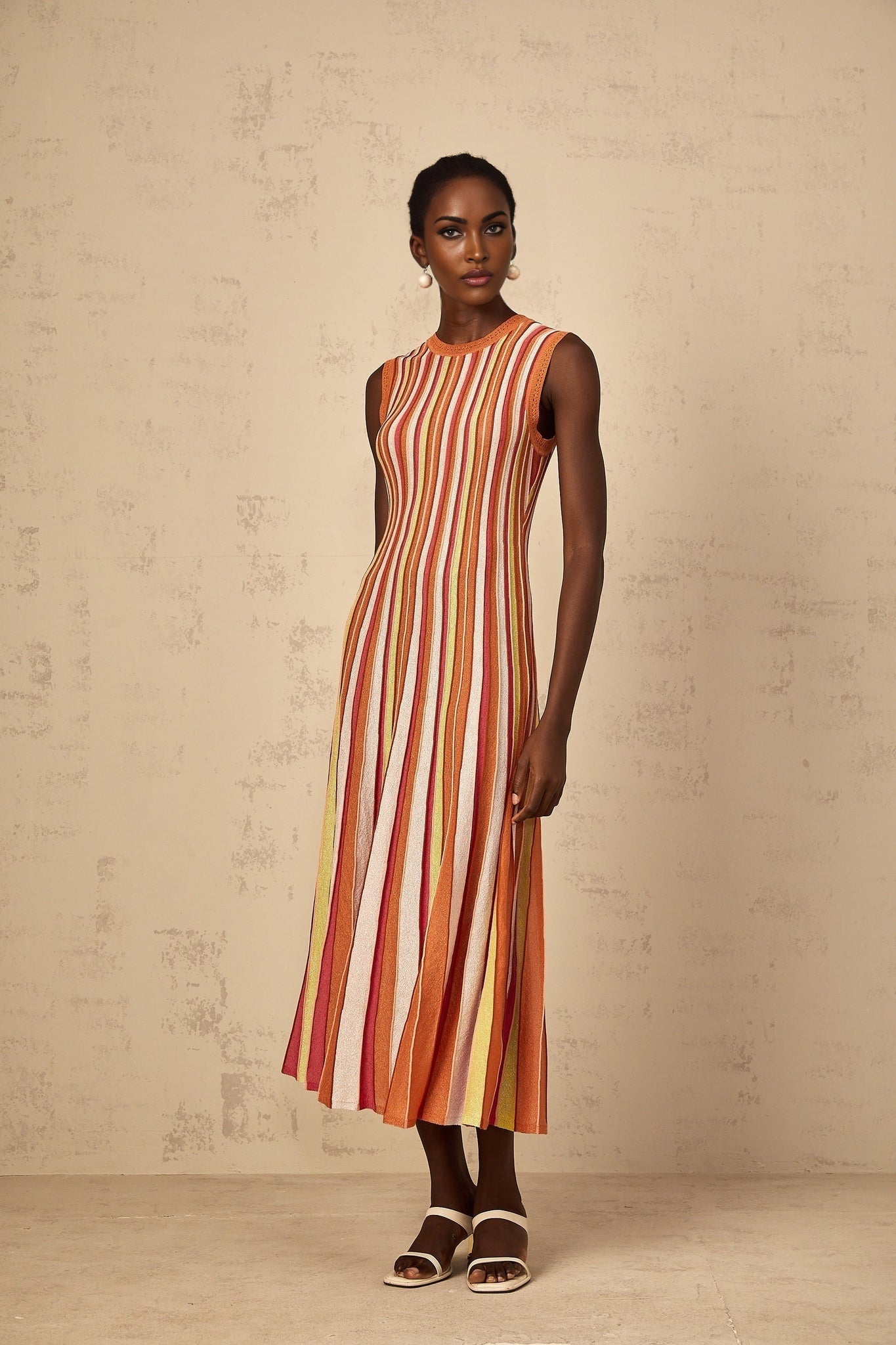 A woman wearing an orange and white vertical striped knit midi dress standing in a relaxed pose