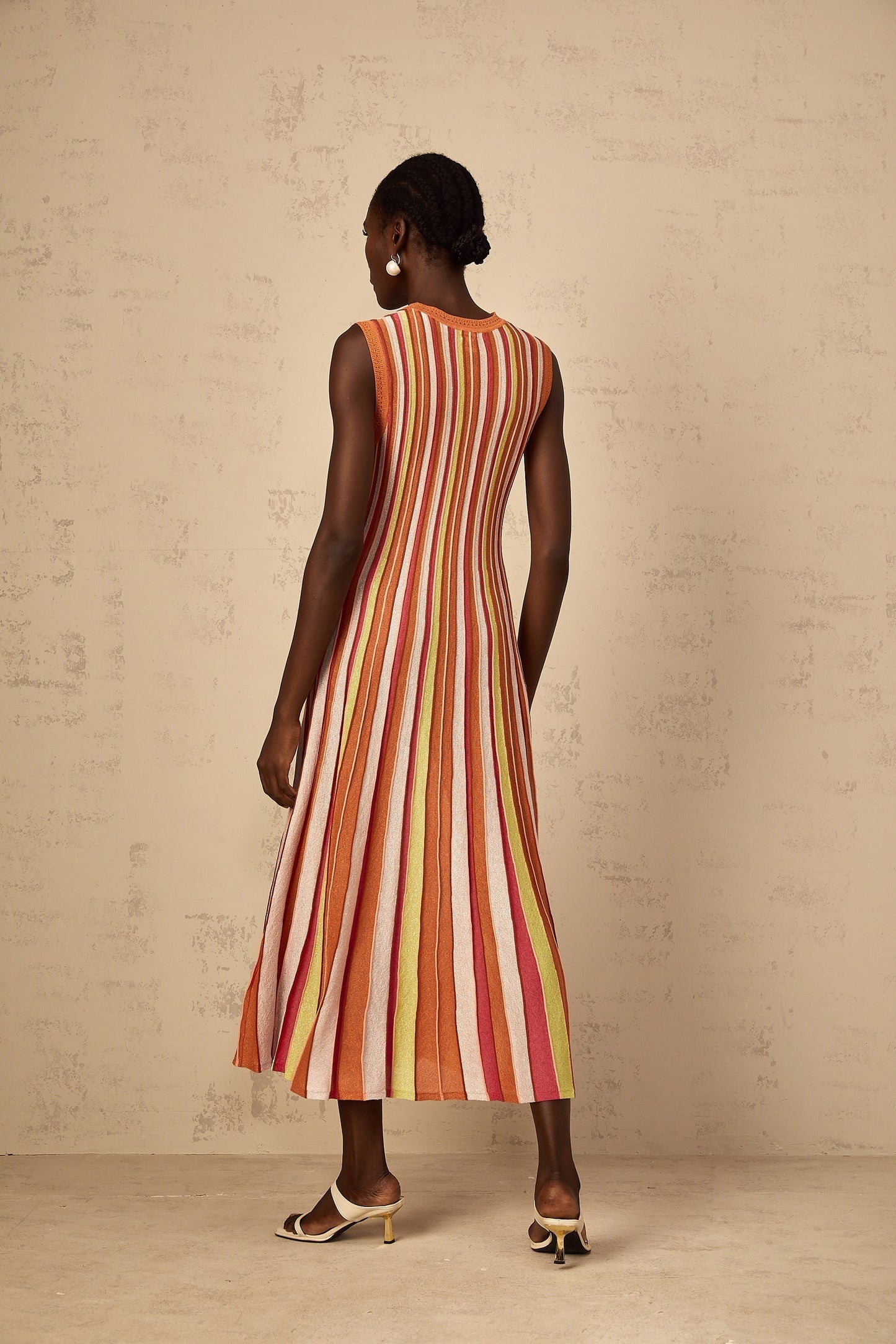 A woman wearing an orange and white vertical striped knit midi dress with a fitted silhouette standing against a plain background