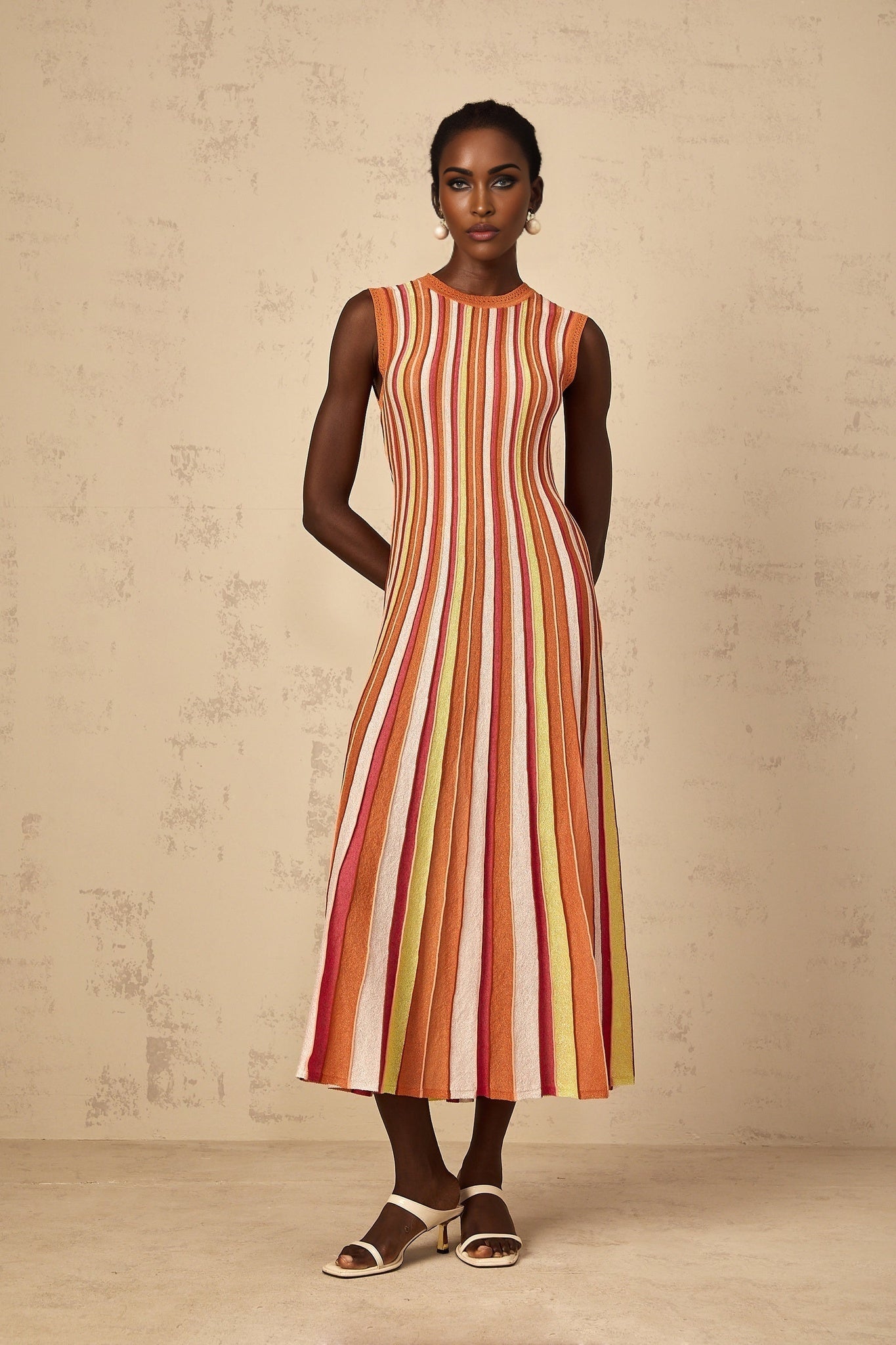 A woman wearing an orange and white vertical striped knit midi dress with long sleeves standing against a plain background