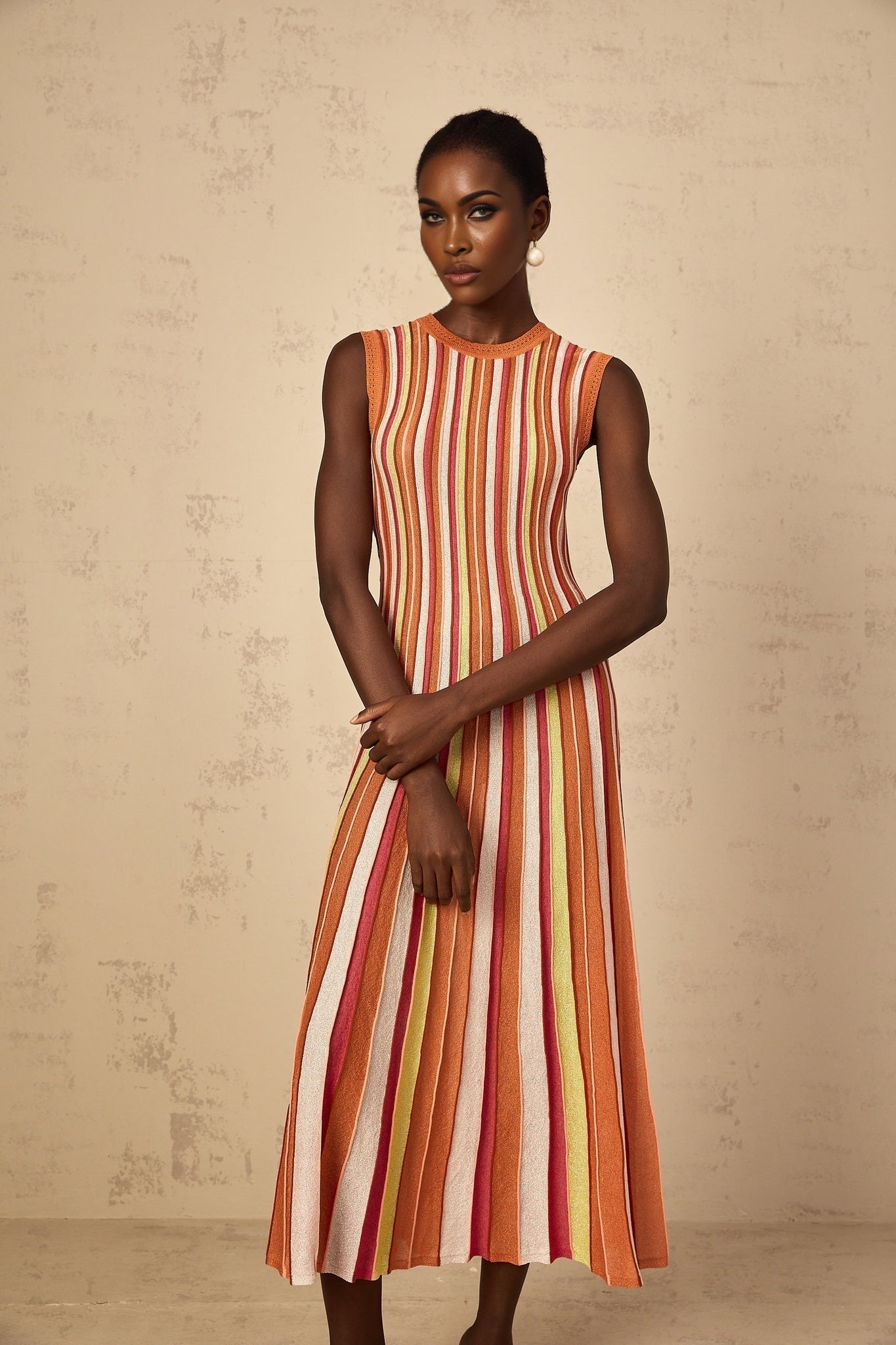 A woman wearing an orange and white vertical striped knit midi dress with long sleeves standing against a plain background