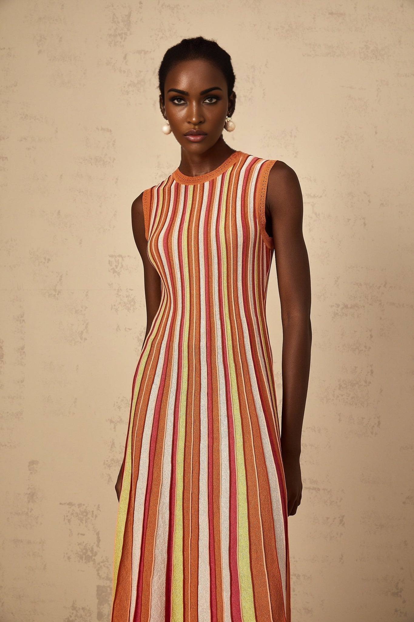 A woman wearing an orange and white vertical striped knit midi dress with long sleeves standing against a plain background