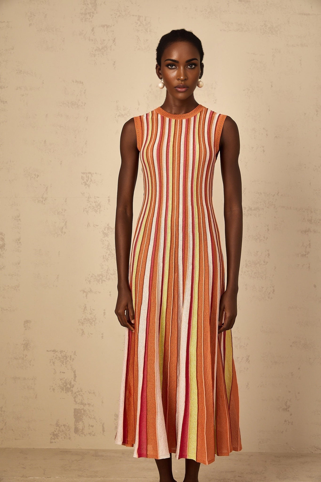 A woman wearing an orange midi dress with vertical white stripes and a knit texture standing in a neutral background