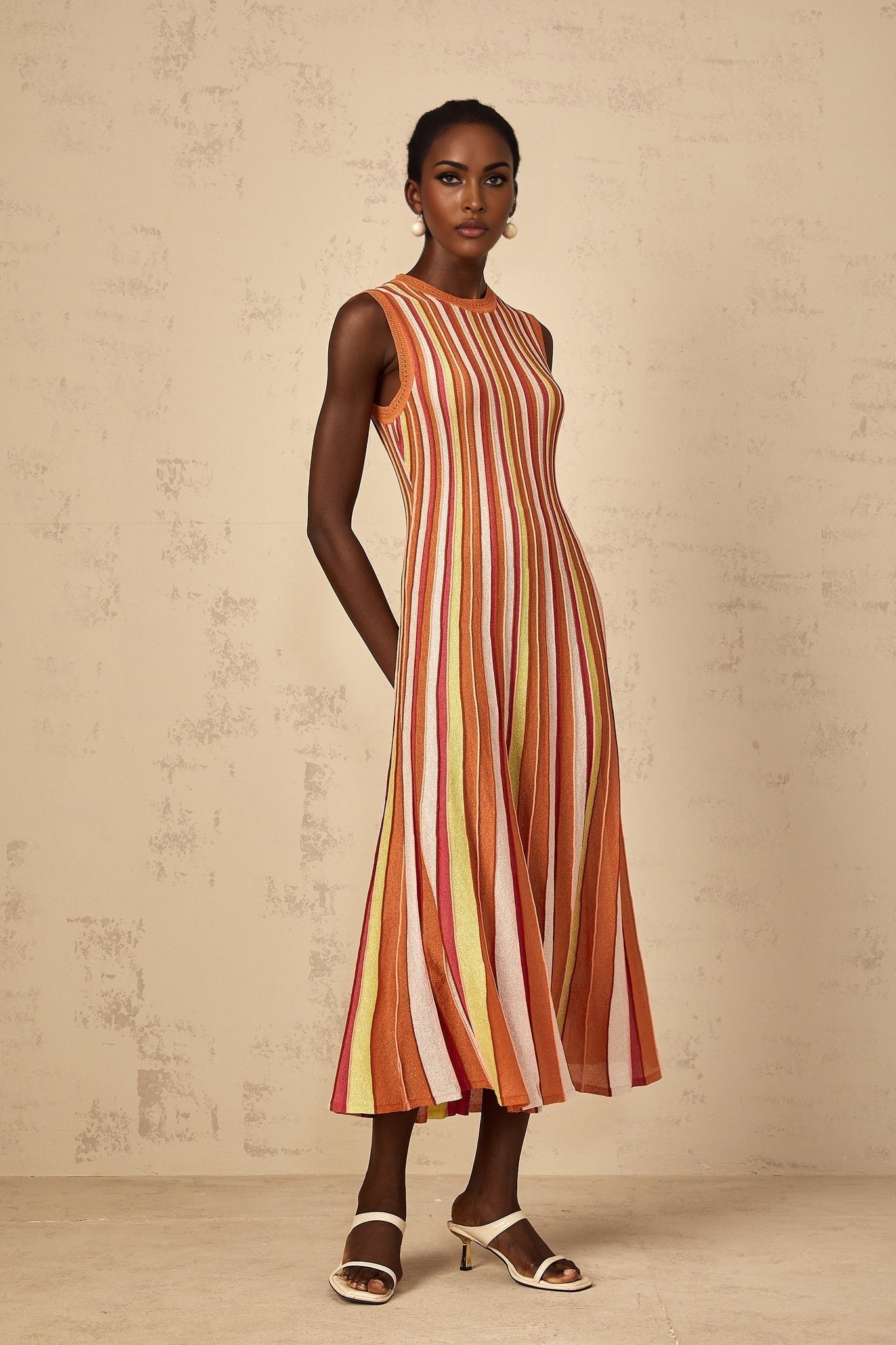 A woman wearing an orange midi dress with vertical white stripes and a knit texture standing in a relaxed pose