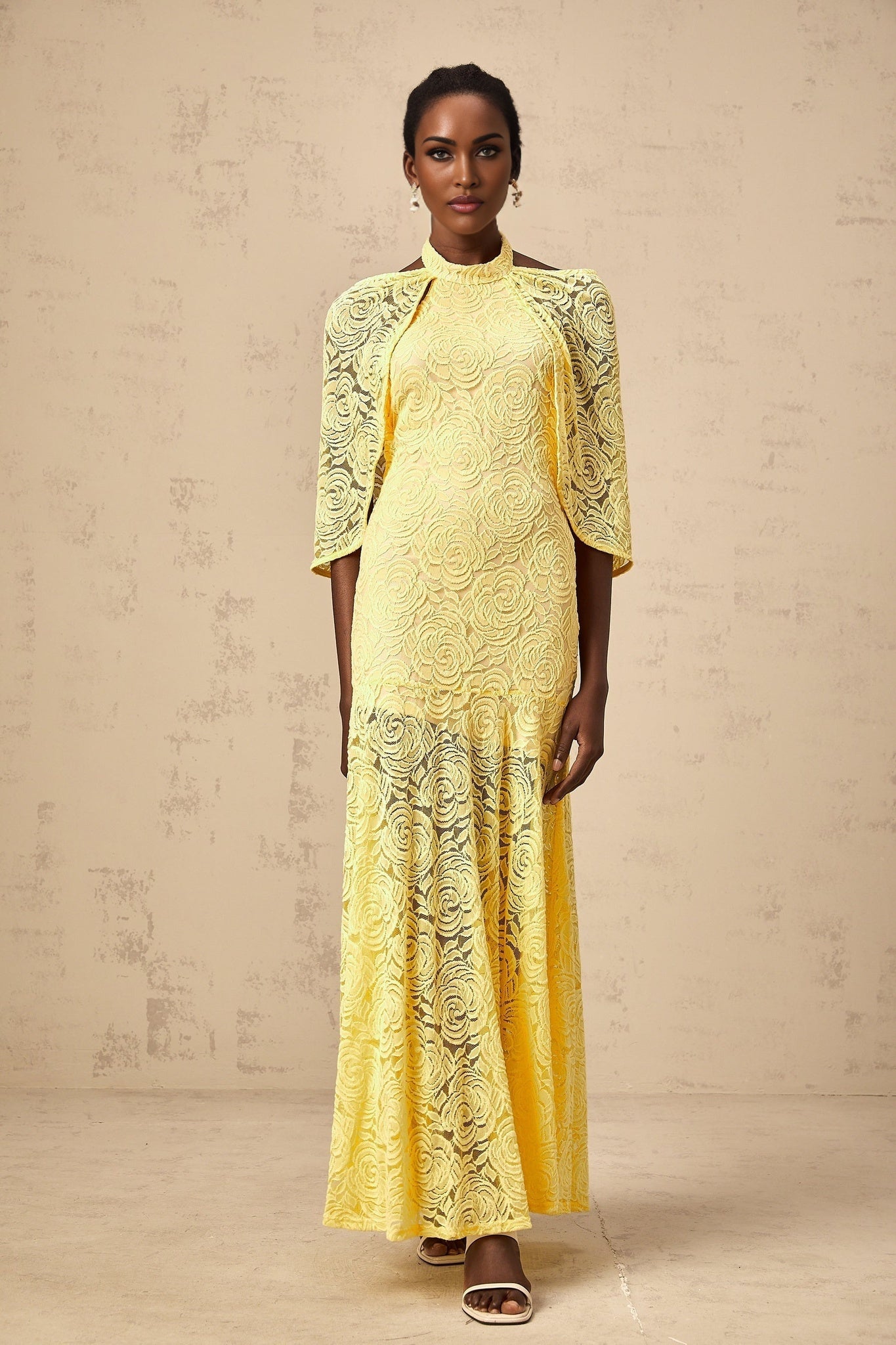 A yellow floorlength dress with a cape design made of delicate chantilly lace featuring a flowy silhouette and intricate lace patterns throughout