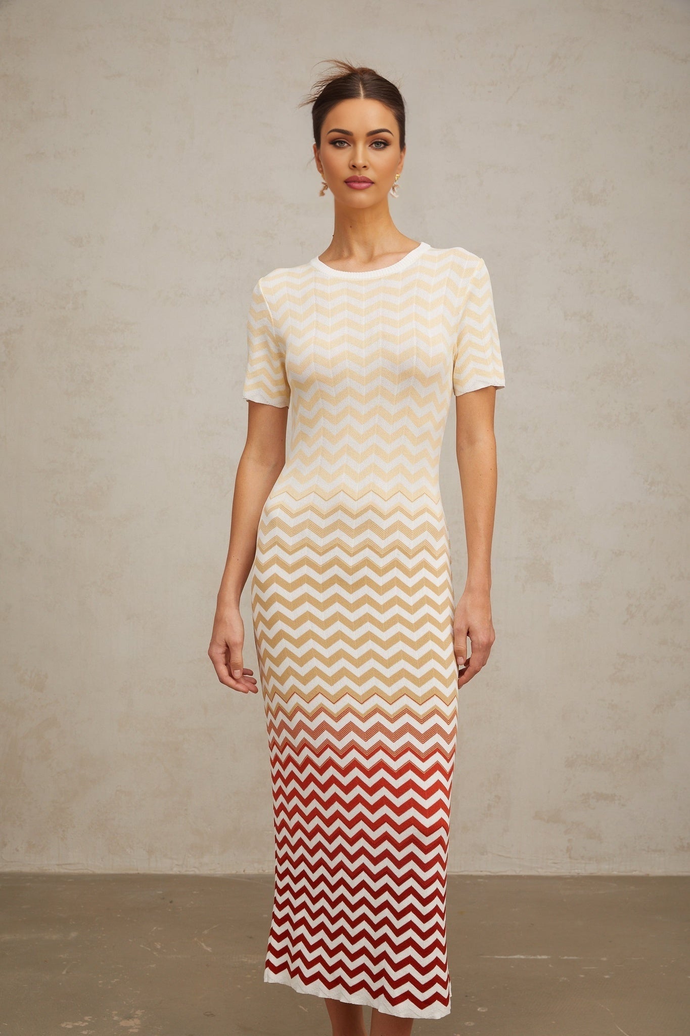 A yellow knit midi dress with a zigzag pattern worn by a model standing against a plain background