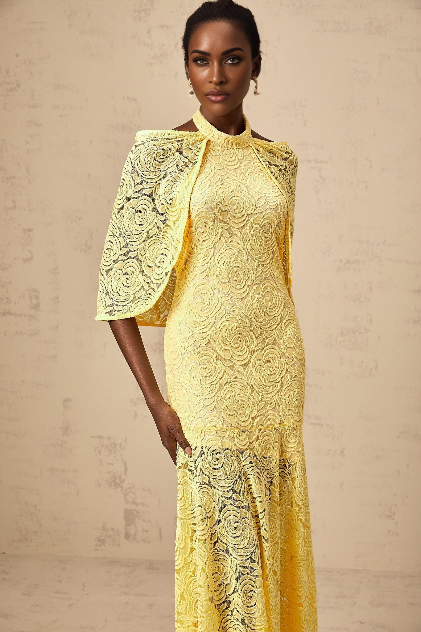 A yellow maxi dress with a cape design made of delicate chantilly lace featuring a long flowing silhouette