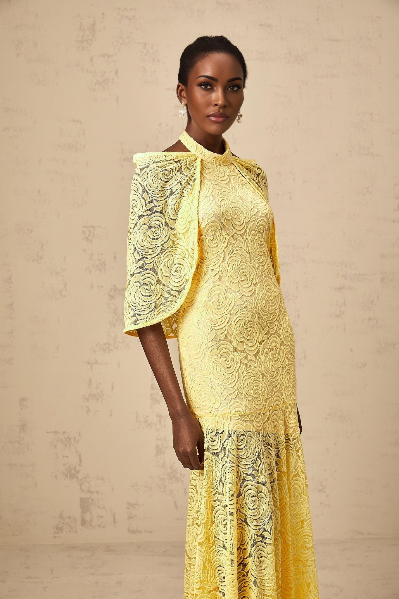A yellow maxi dress with a cape design made of delicate Chantilly lace featuring an elegant and flowing silhouette