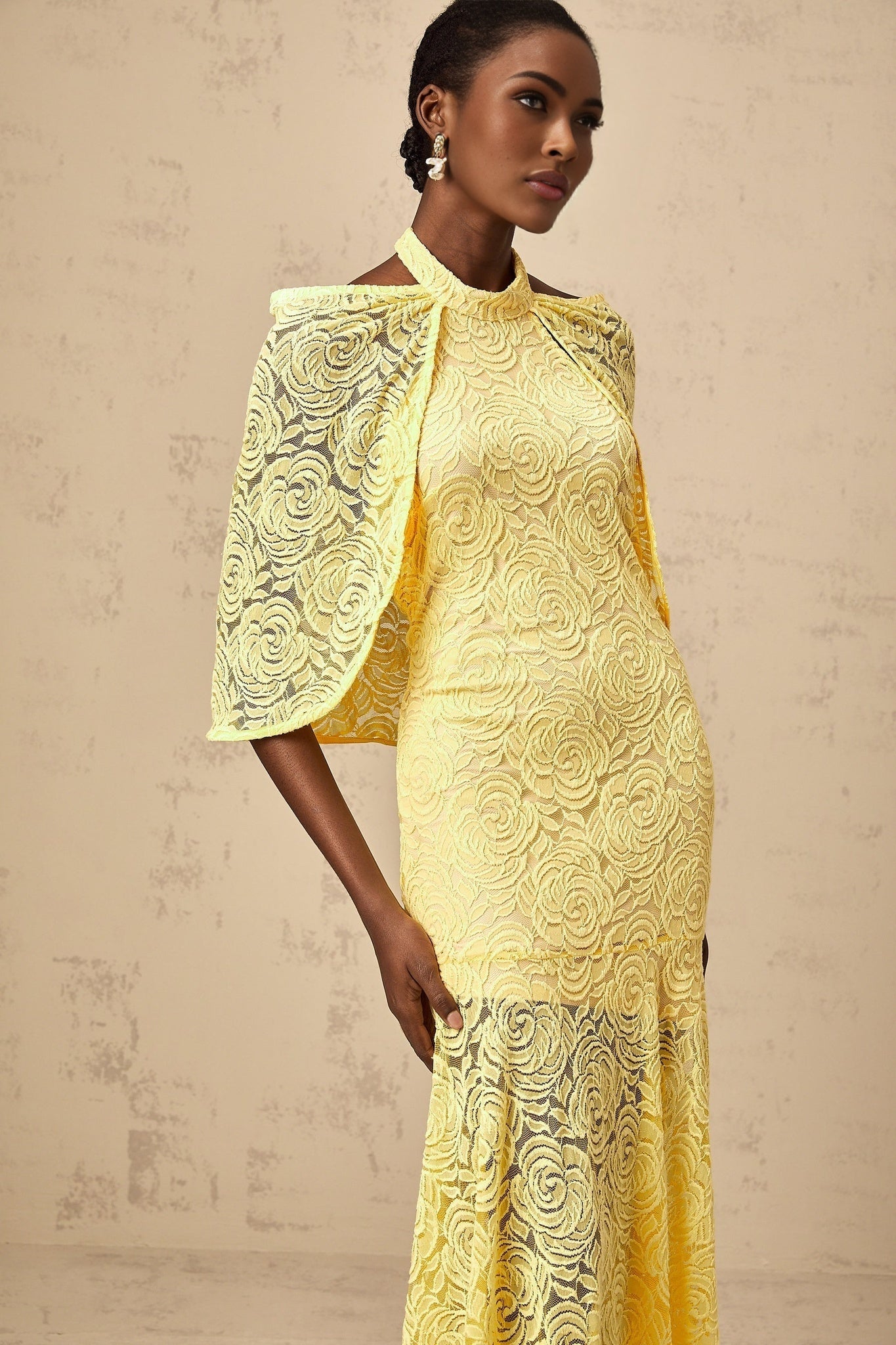 A yellow maxi dress with cape design made from chantilly lace featuring an elegant and flowing silhouette