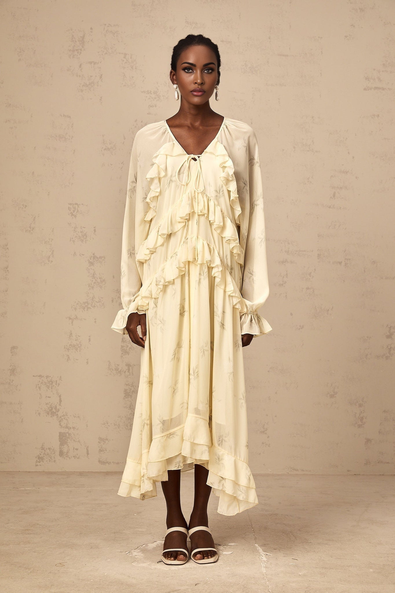 A yellow midi dress with a floral print pattern made of chiffon fabric featuring ruffle details and a flowing silhouette