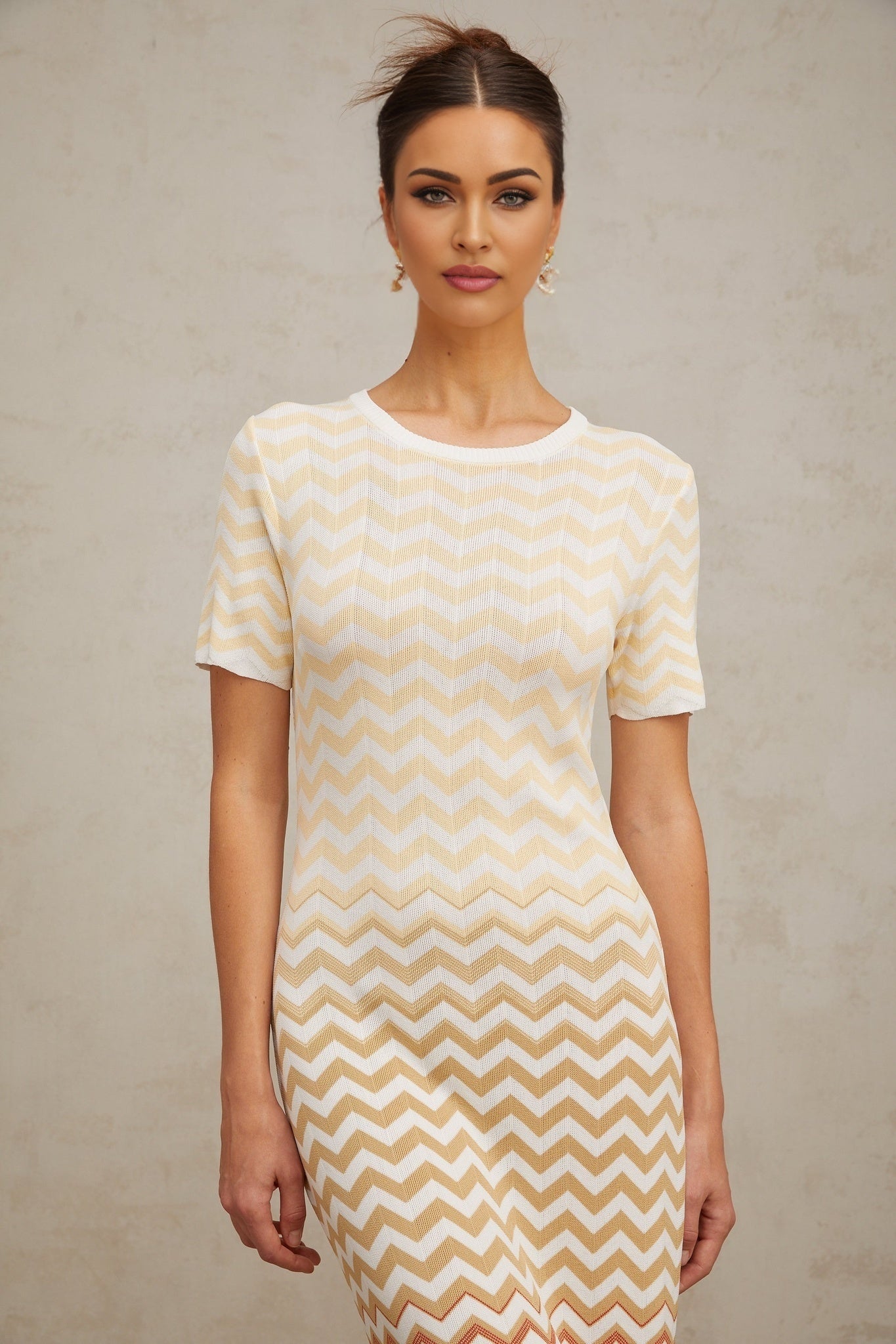 A yellow midi dress with a zigzag knit pattern worn by a model standing against a plain background