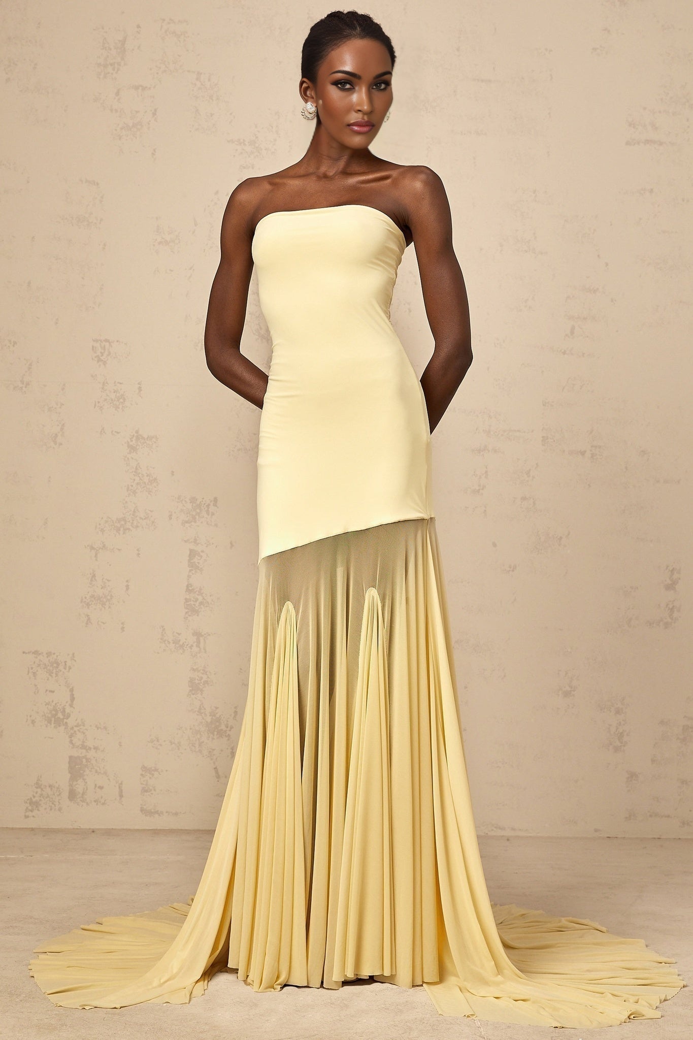 A yellow offshoulder maxi dress with sheer tulle fabric flowing to the floor worn by a model against a plain background