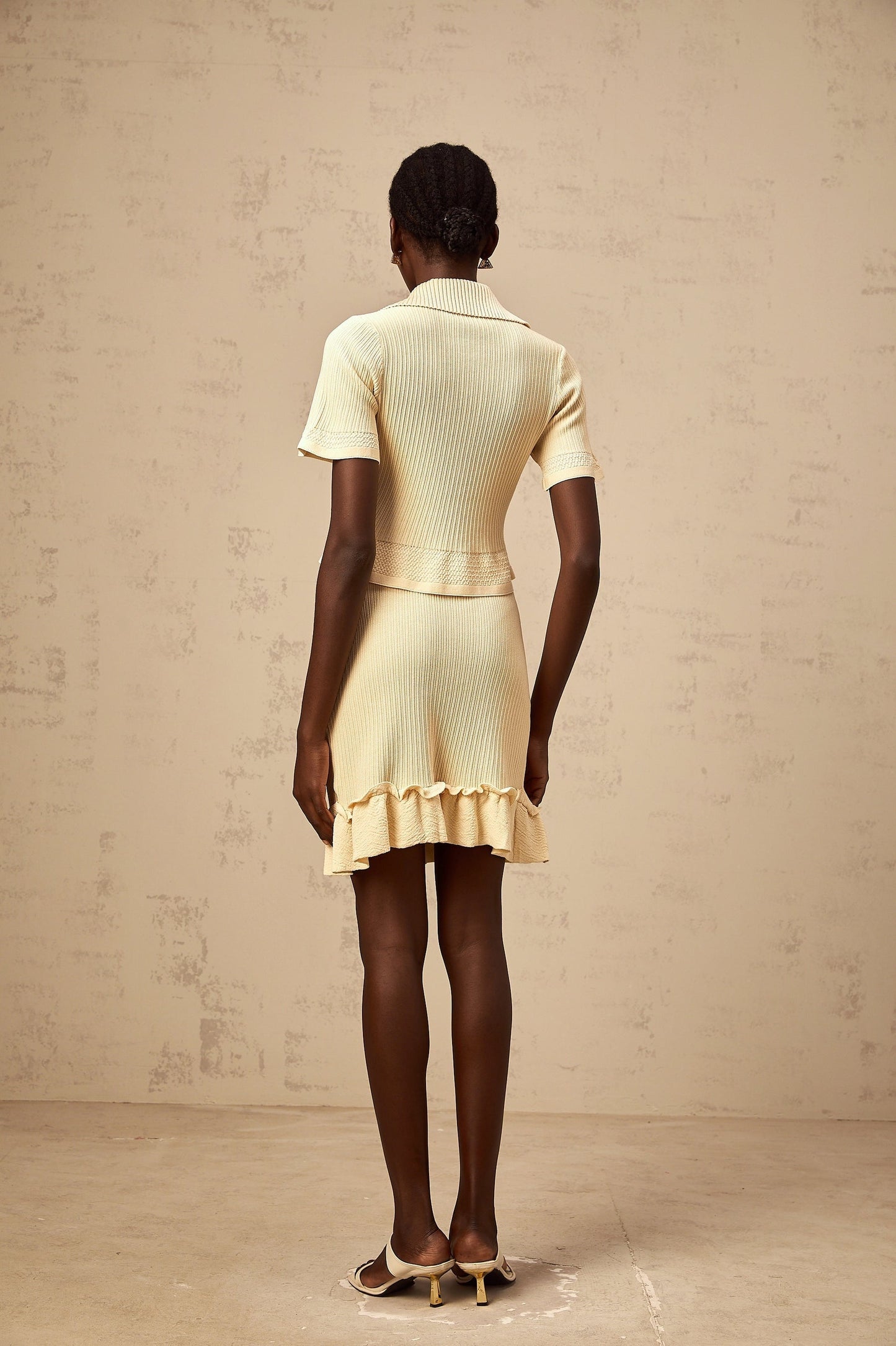 A yellow ribbed knit matching set consisting of a ruffled top and skirt The top features ruffled details while the skirt is form fitting Both pieces are made from a textured ribbed fabric in a bright yellow color