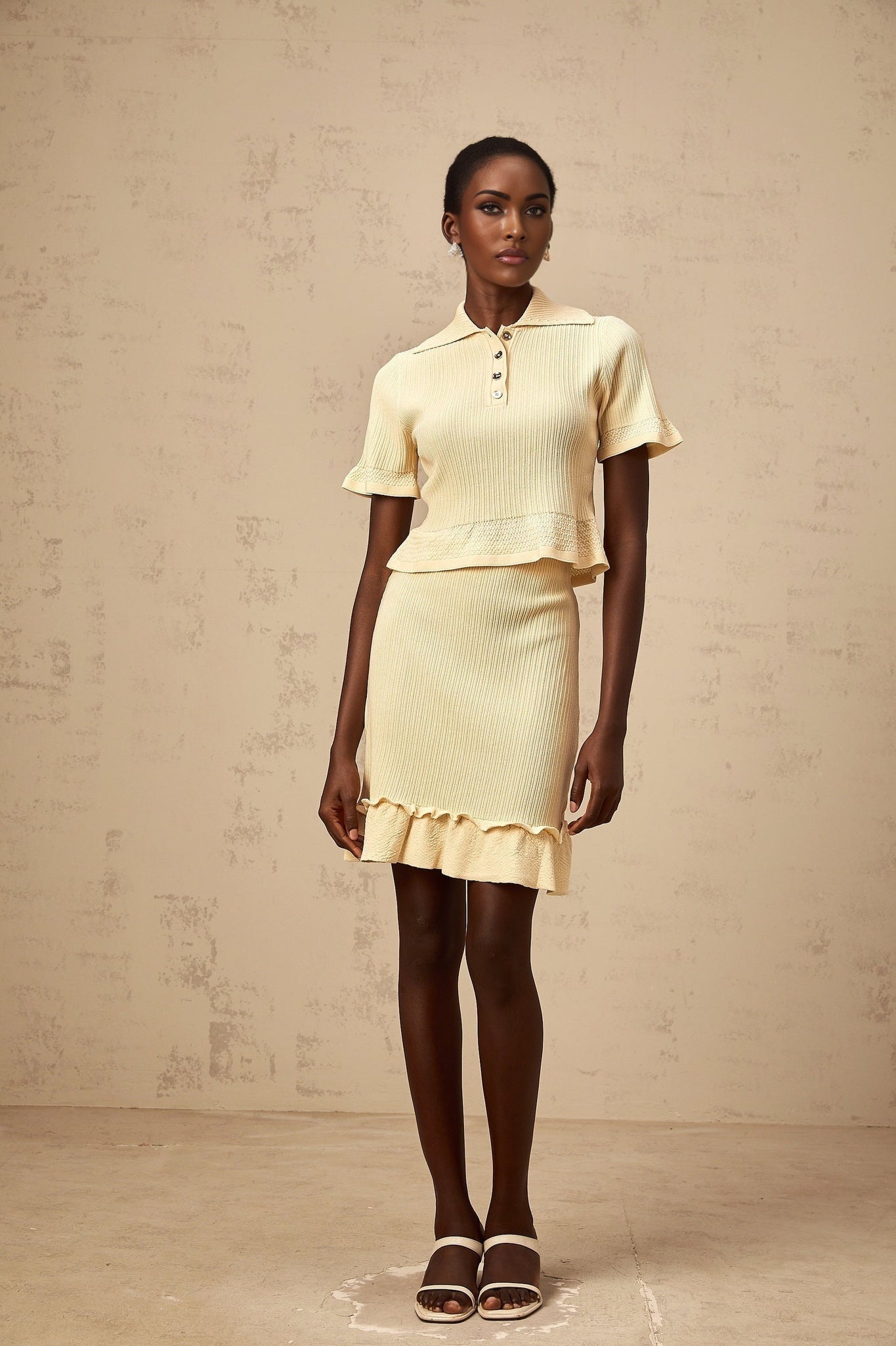A yellow twopiece outfit consisting of a ruffled ribbed knit top and matching skirt both in a bright sunny shade The top features ruffles along the neckline and sleeves while the skirt has a fitted silhouette creating a coordinated and feminine look