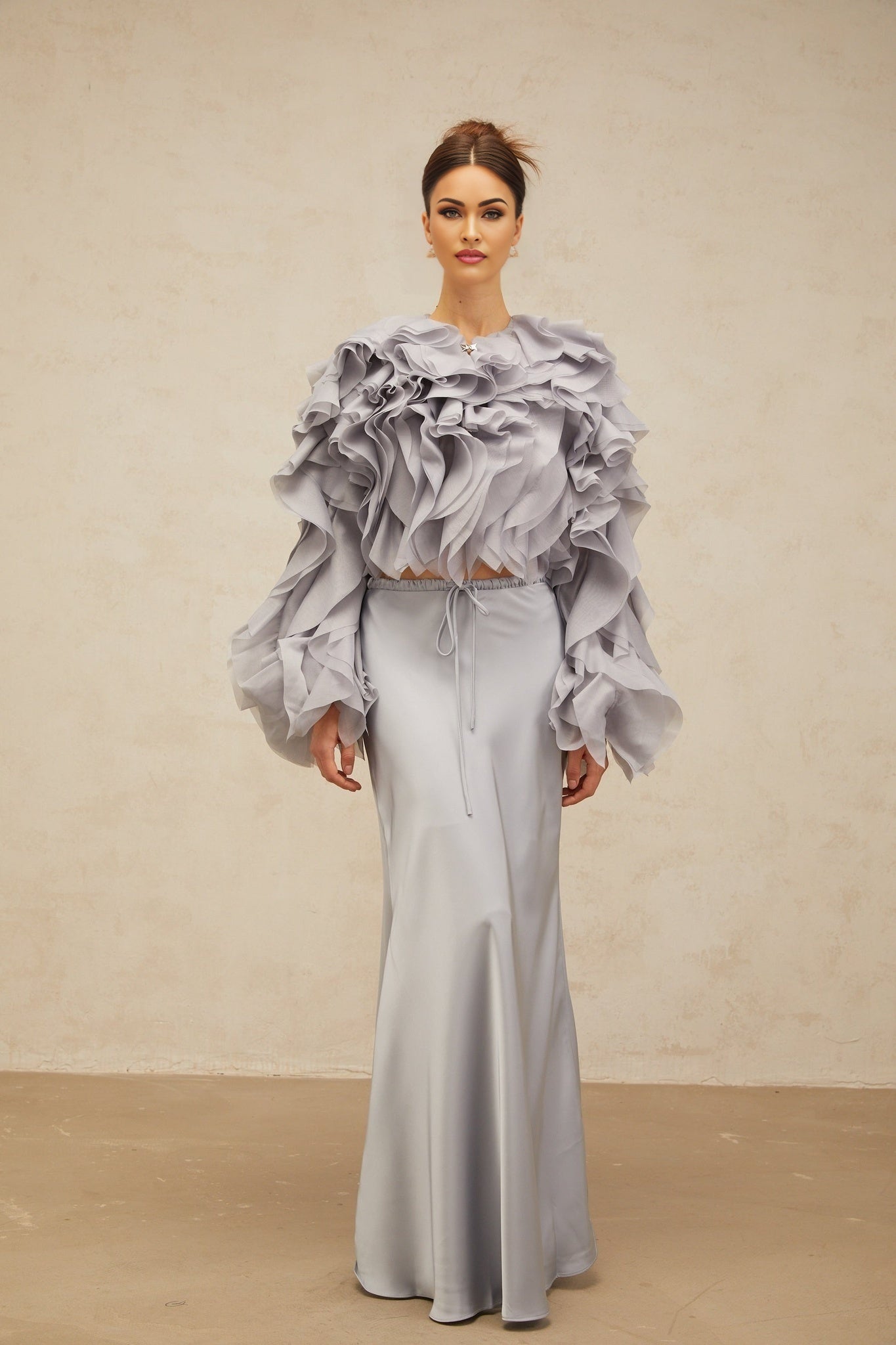 A young girl wearing a light blue blouse with a large bow and ruffled details paired with a matching skirt in the same color creating a coordinated outfit set